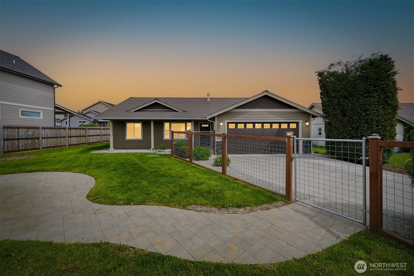 Front view of a modern suburban house with a driveway, outdoor lighting, and a fenced yard during sunset in Ferndale WA