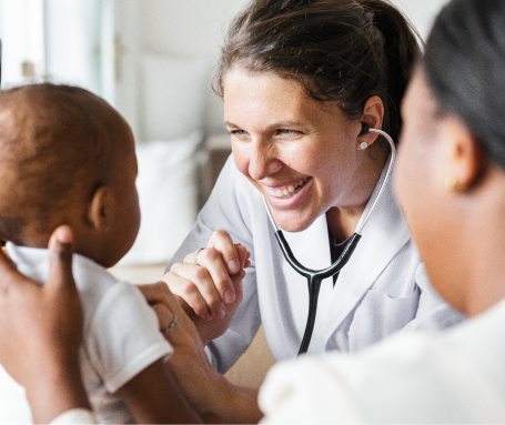 A female healthcare professional smiling and talking to a young patient with a stethoscope around her neck.