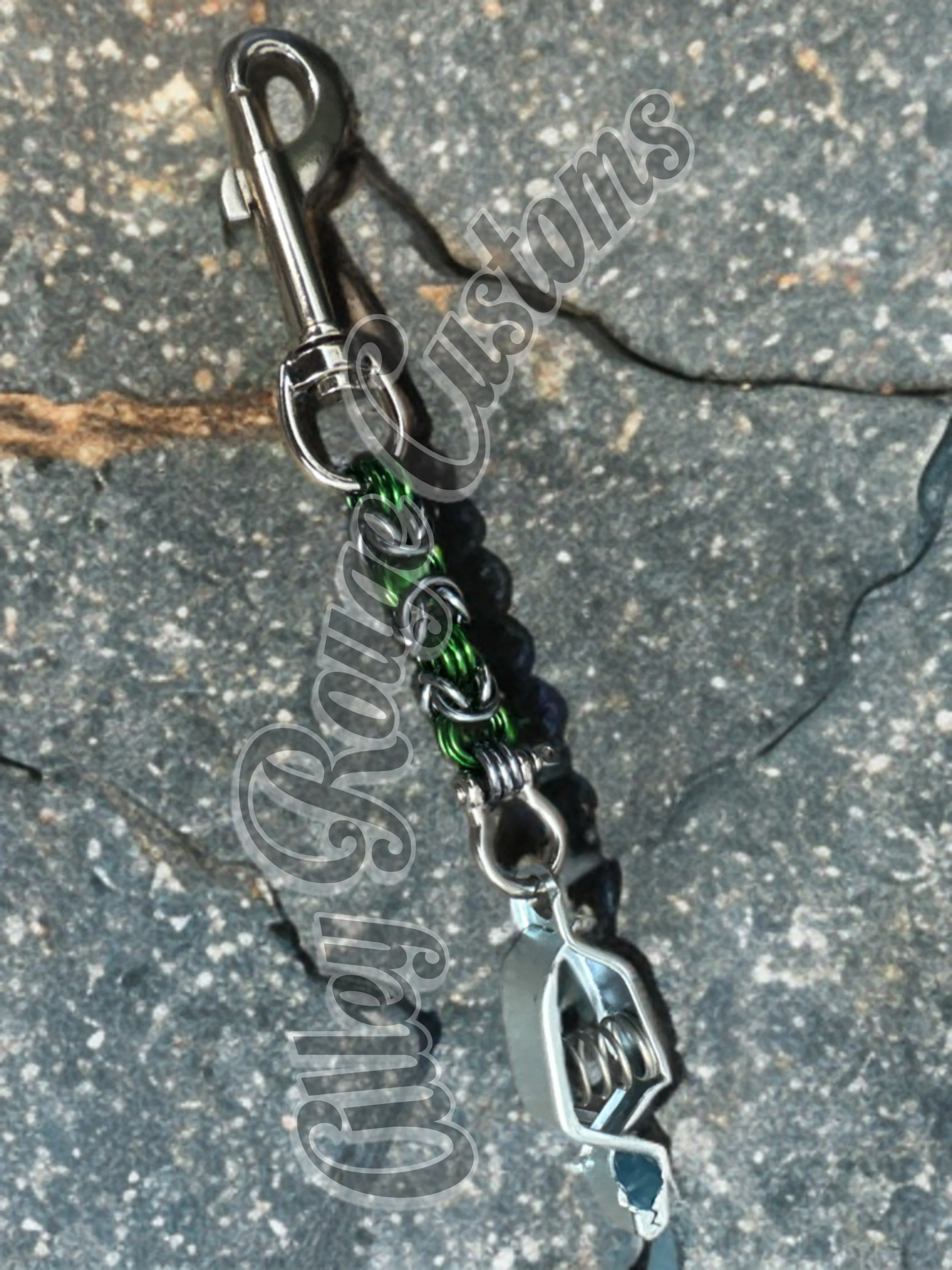 A rock climbing carabiner gear with metal carabiner and various black, green, and silver climbing tools and straps on a rough outdoor surface.