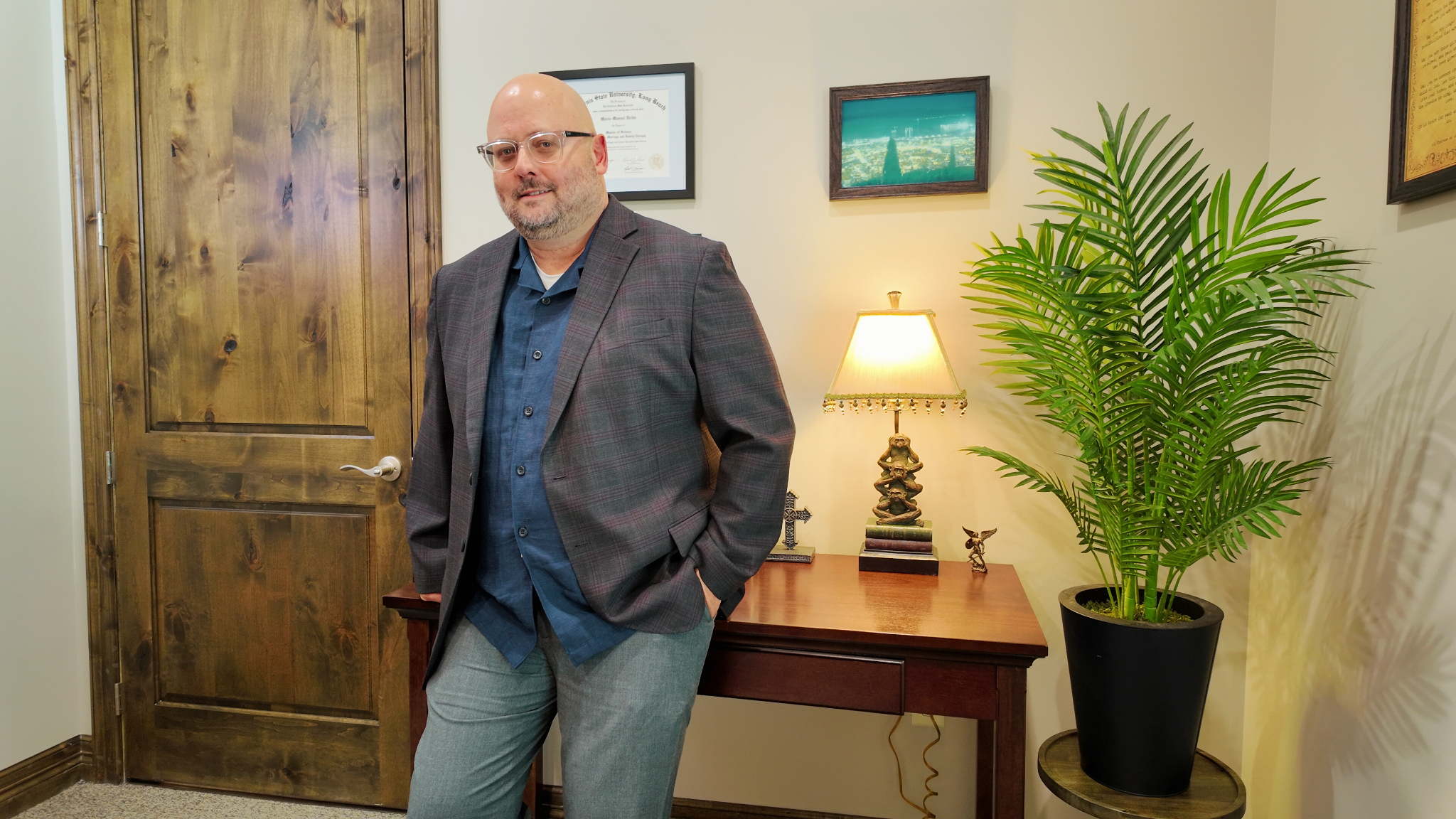 Mario Uribe stands in his office with a gray blazer, a blue shirt, and gray pants to welcome people to his practice.