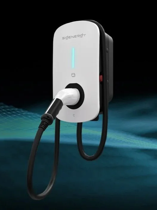 Electric vehicle charging station with a white front panel and black sides, showing a lit vertical indicator, a cable with a connector inserted into the port.