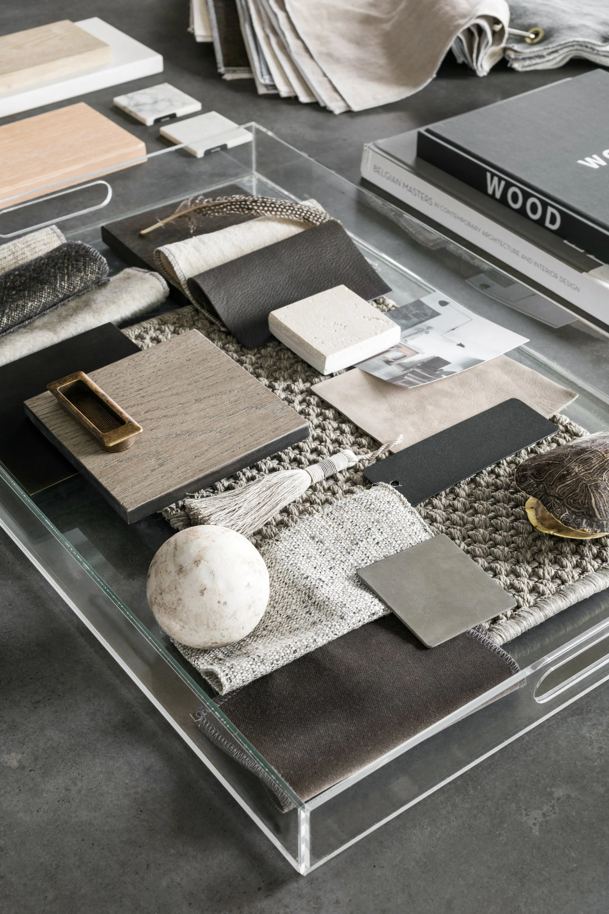 A curated selection of interior design samples on a glass table, including fabric swatches, wood and tile samples, a shell, and design books.