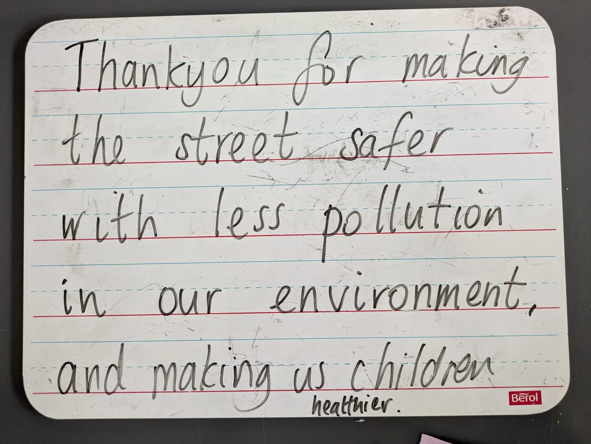 A photo of an erasable whiteboard with text written on it: "Thank you for making the street safer with less pollution in our environment, and making us children healthier."