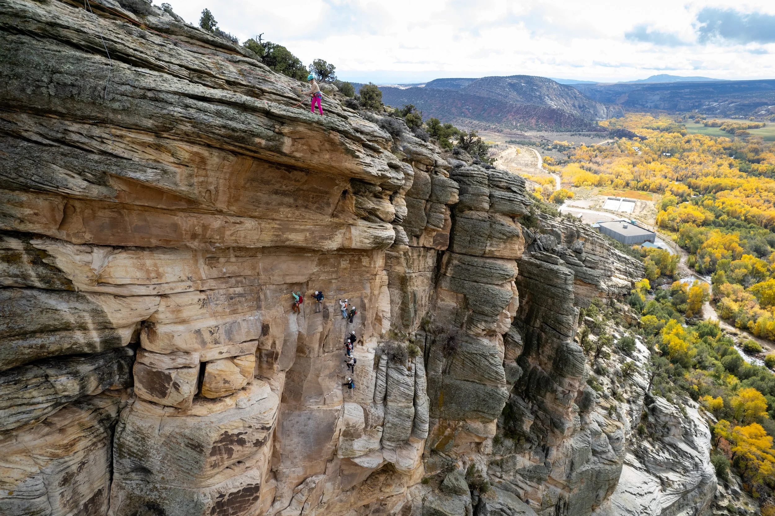 A climber pauses on a rock ledge overlooking Ashley Gorge Canyon and the valley below
