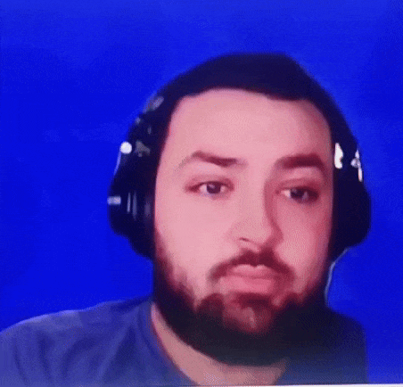 A man with dark hair and beard wearing headphones, sitting in front of a blue background.