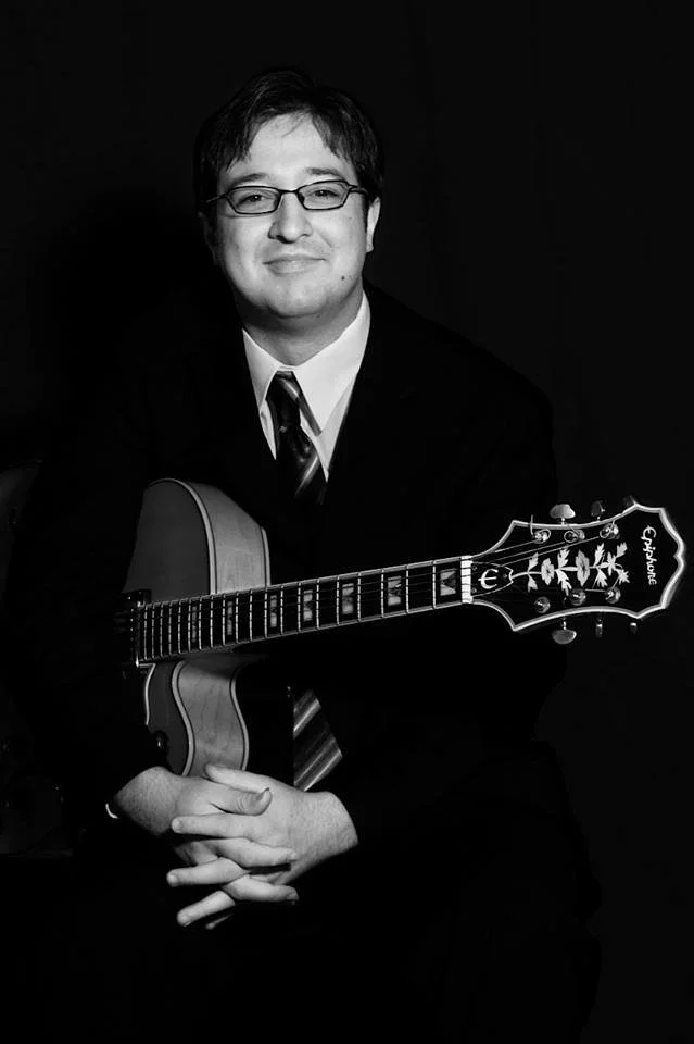 Black and white photo of musician Daniel Keller holding his guitar