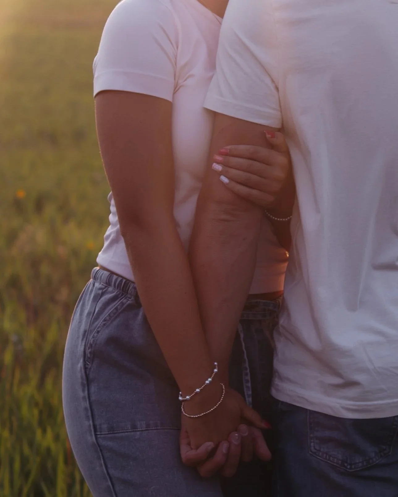 A close-up of two people holding hands and embracing outdoors during sunset, with a blurred natural background.