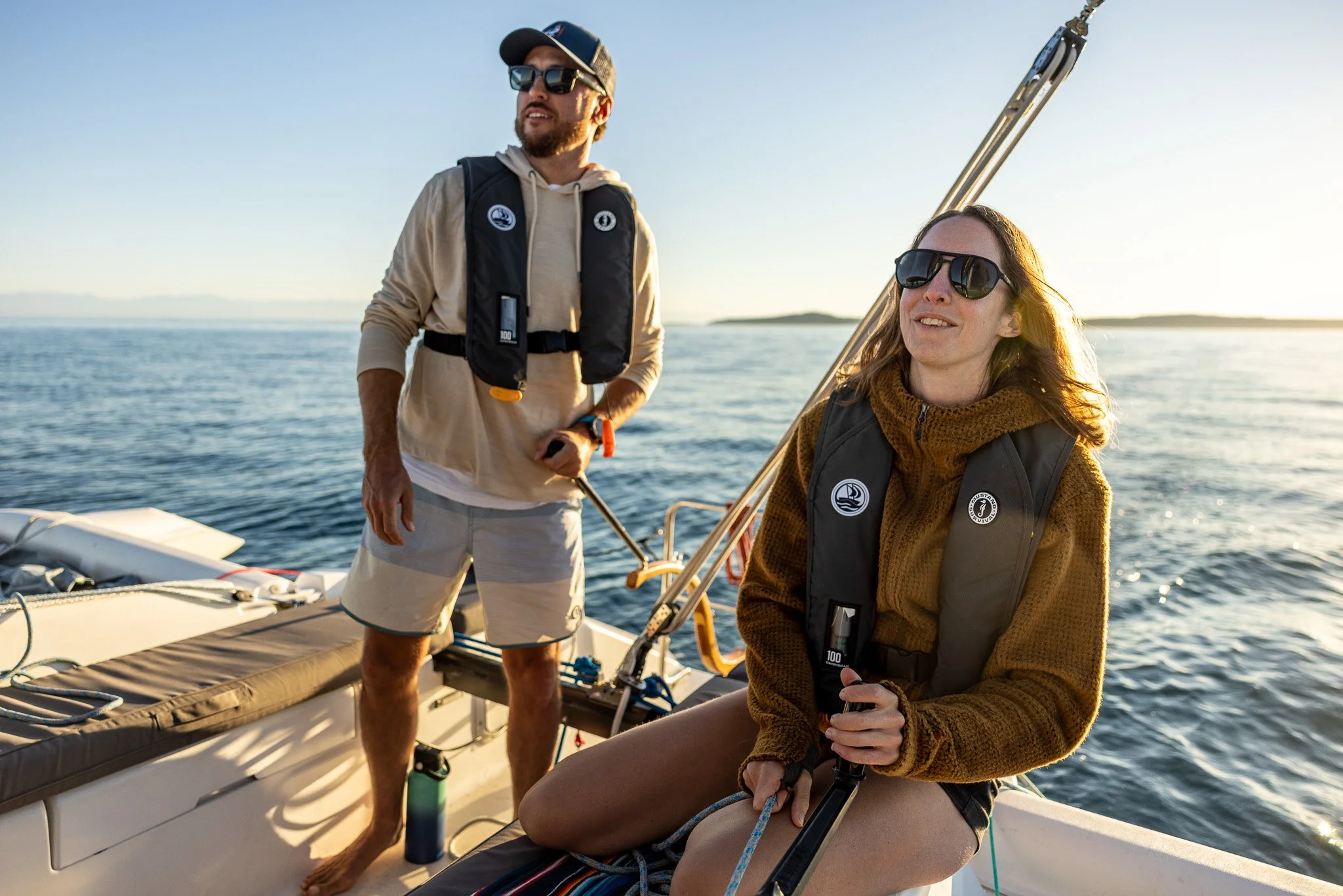 Two women sitting on a boat deck, relaxing by the water with a distant shoreline and trees, enjoying a sunny day In Penn Cove. 