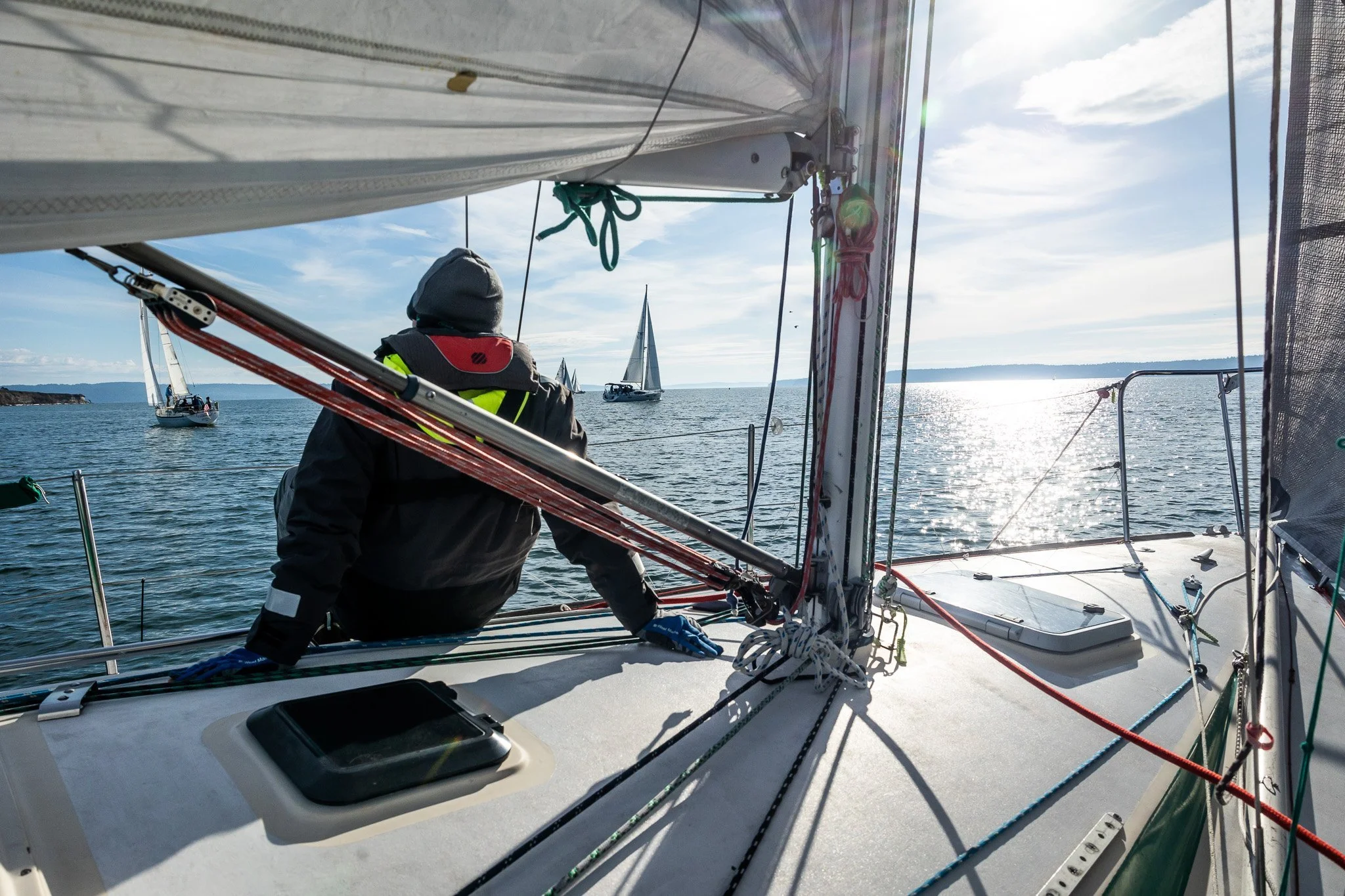 A person on a sailing boat facing the water with sailboats in the distance on a sunny day.