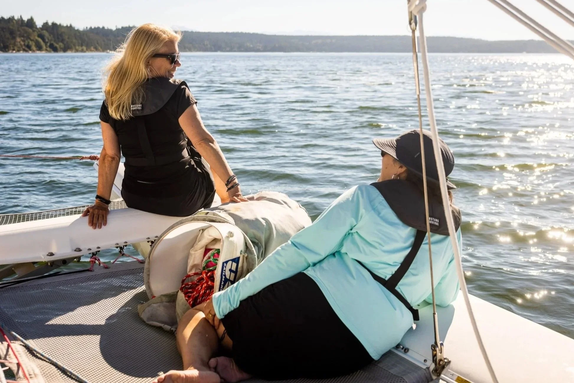 A red wooden building on a pier over water, with people walking and a sailboat docked nearby at the Coupeville pier.