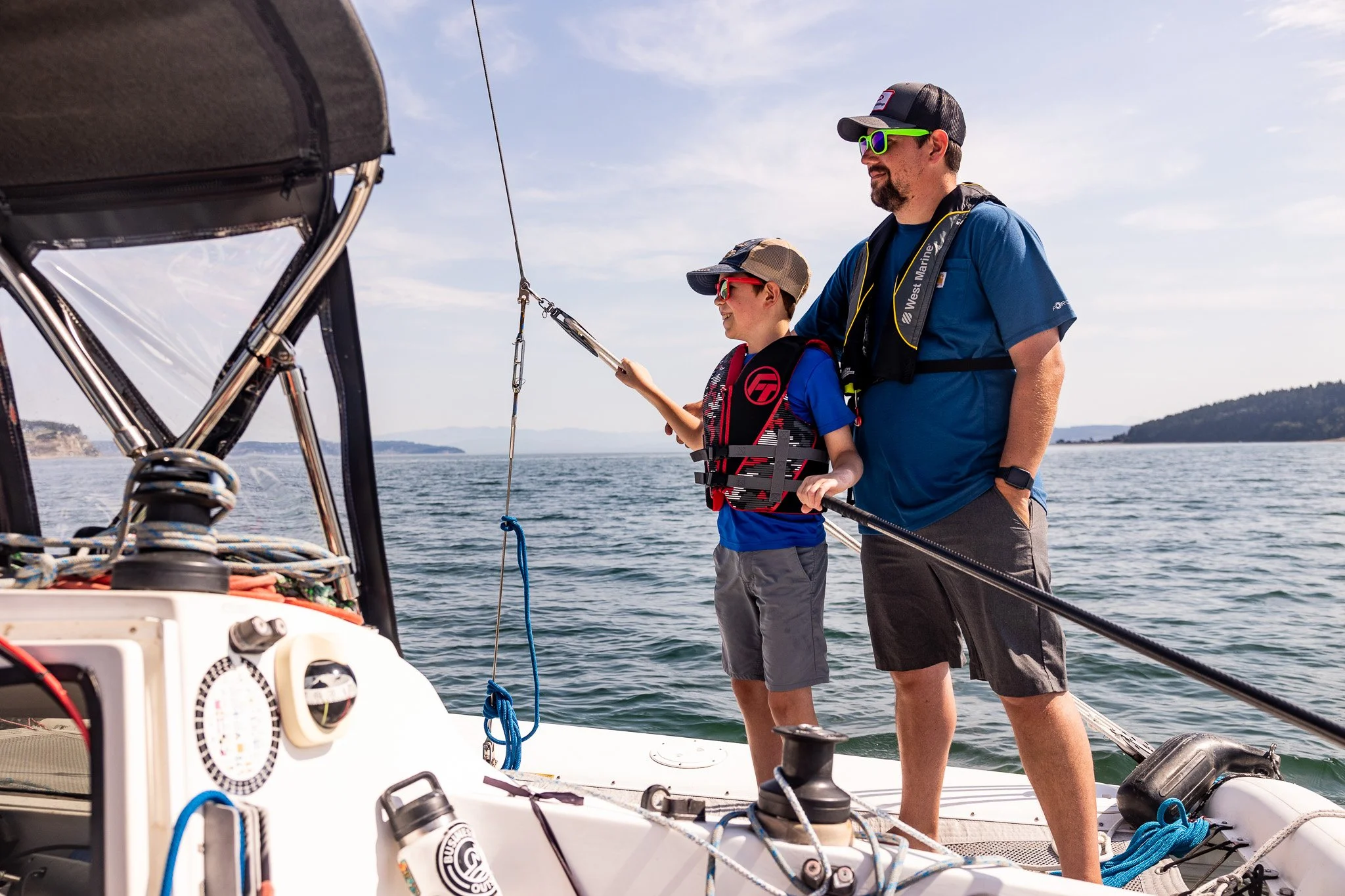 A red wooden building on a pier over water, with people walking and a sailboat docked nearby at the Coupeville pier.