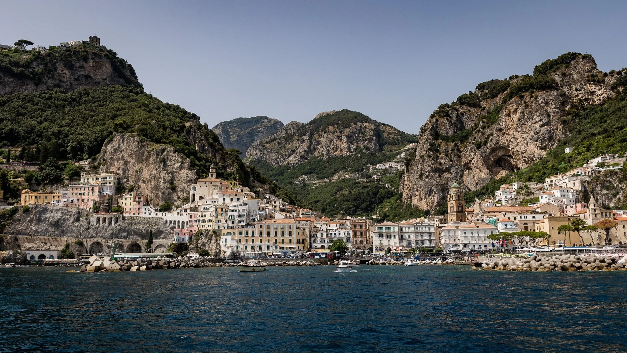 Harbor view of colorful Italian seaside town with hillside buildings and mountainous backdrop.