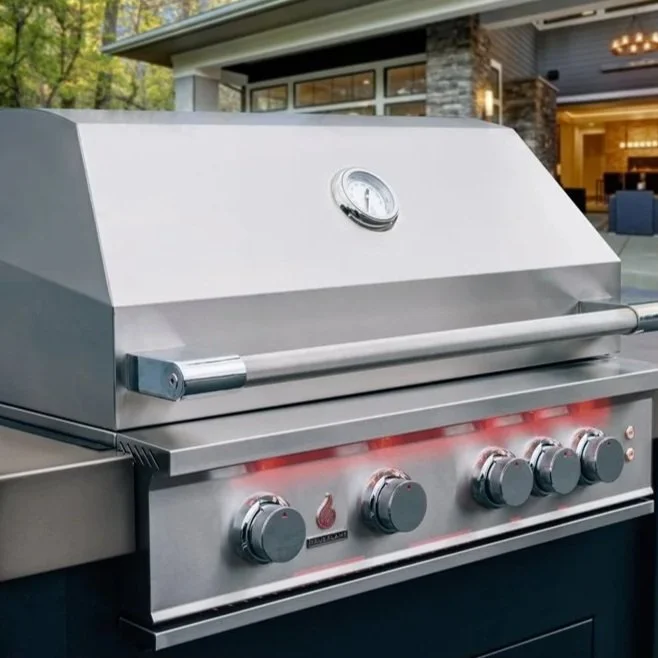 Stainless steel outdoor gas grill with temperature gauge and control knobs, positioned in a backyard patio area.