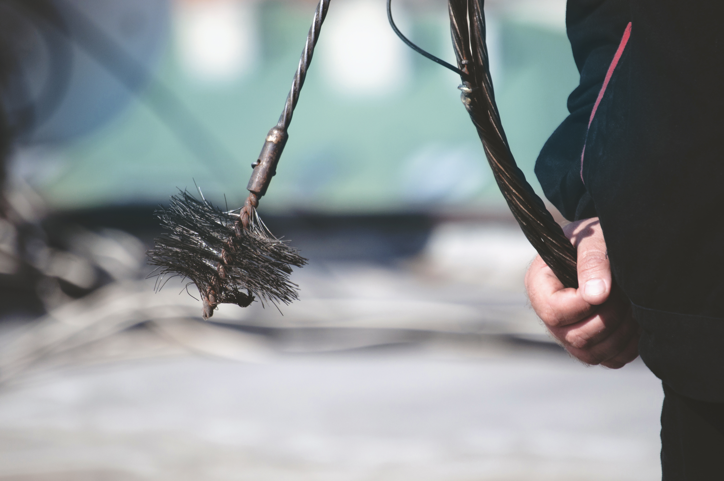 Close-up of a person holding and swinging a wire brush used for cleaning or polishing, with a blurred background.