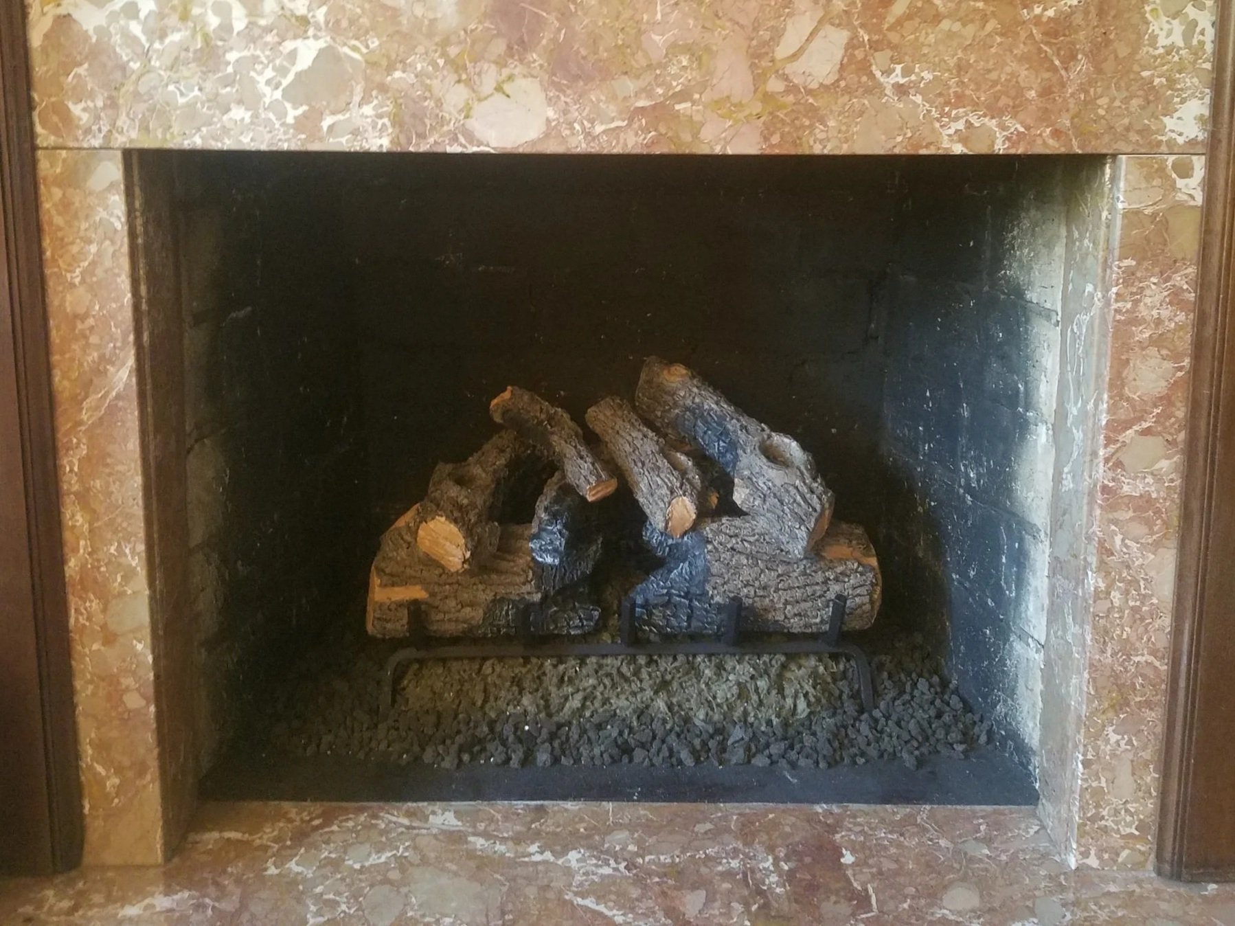 Inside view of a fireplace with stacked logs and a marble surround.