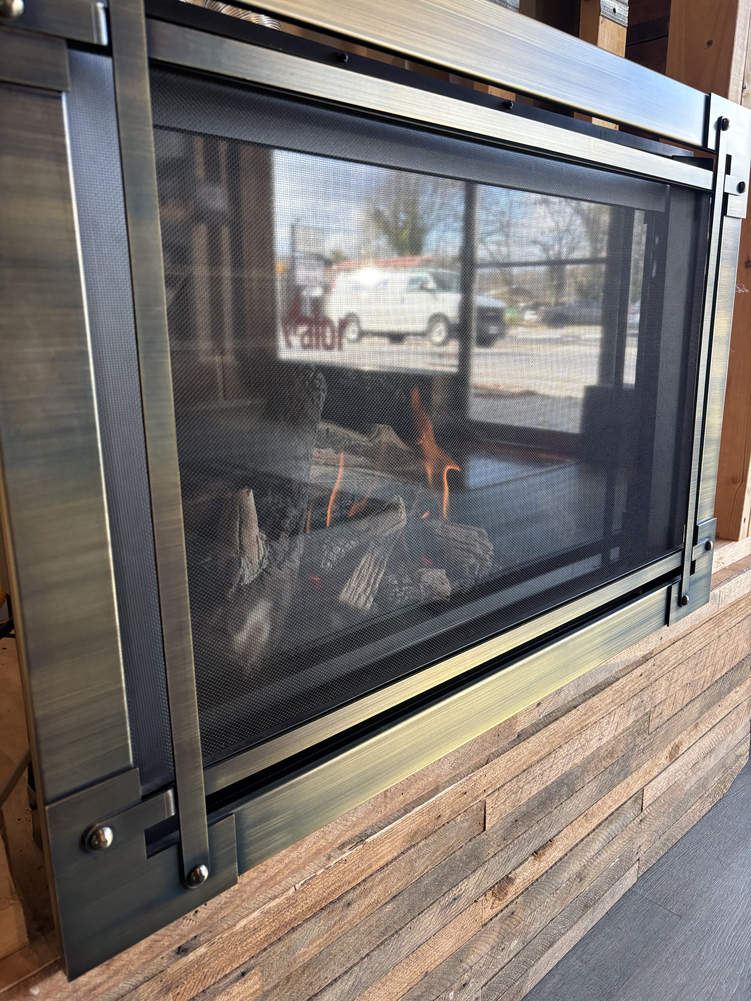 Indoor fireplace with glass front showing logs burning inside, mounted on a wooden wall.