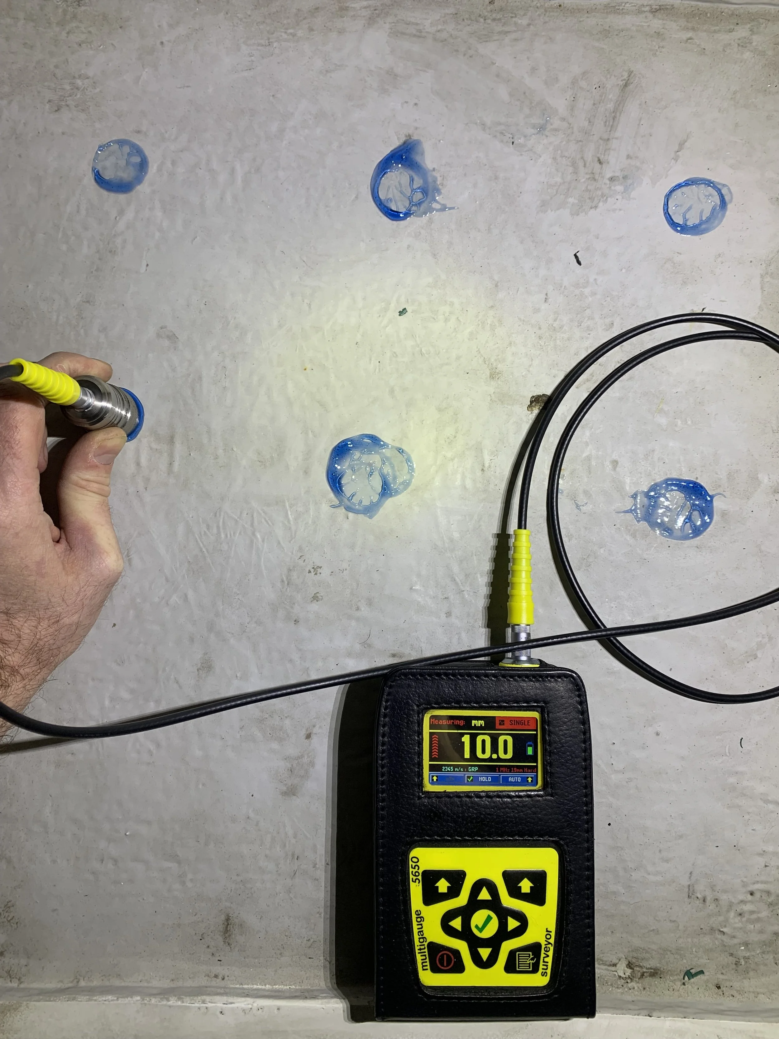 An ultrasonic thickness gauge measuring 10.0 on a digital display. 