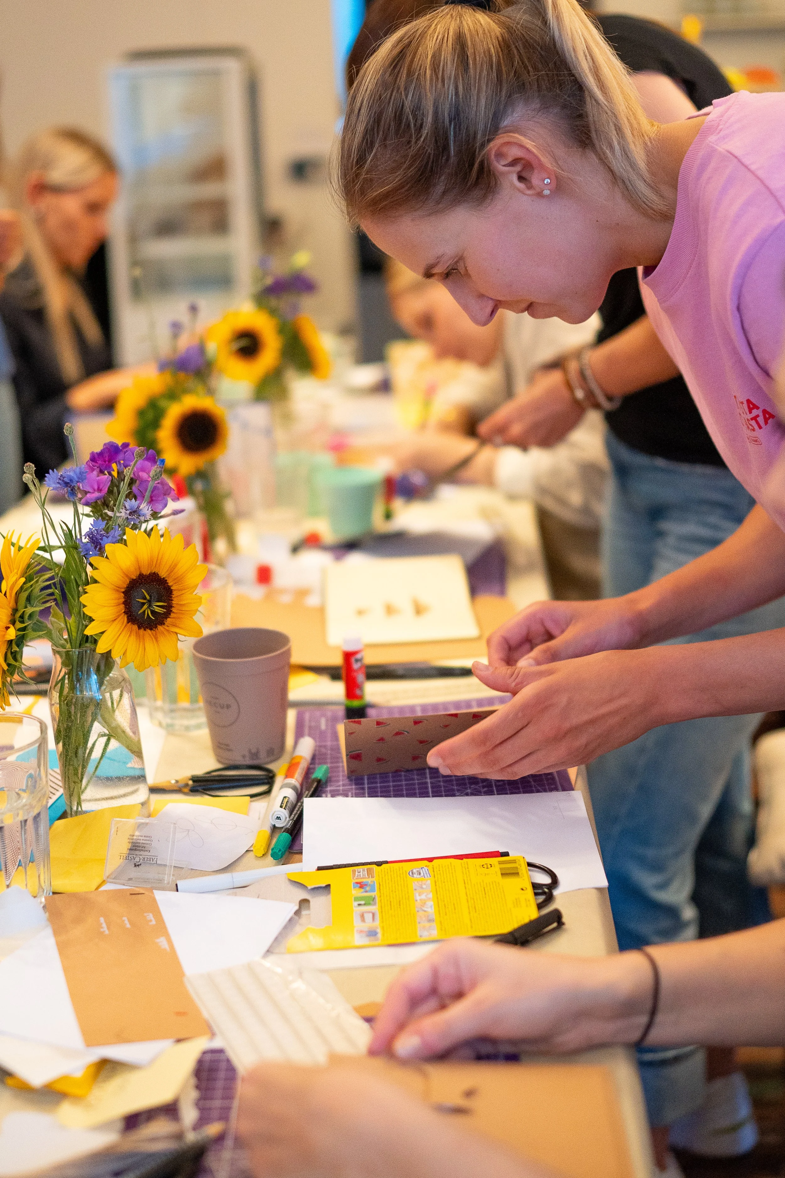 Menschen beim Basteln an einem Tisch mit Blumen, Bastelmaterial und Werkzeugen.
