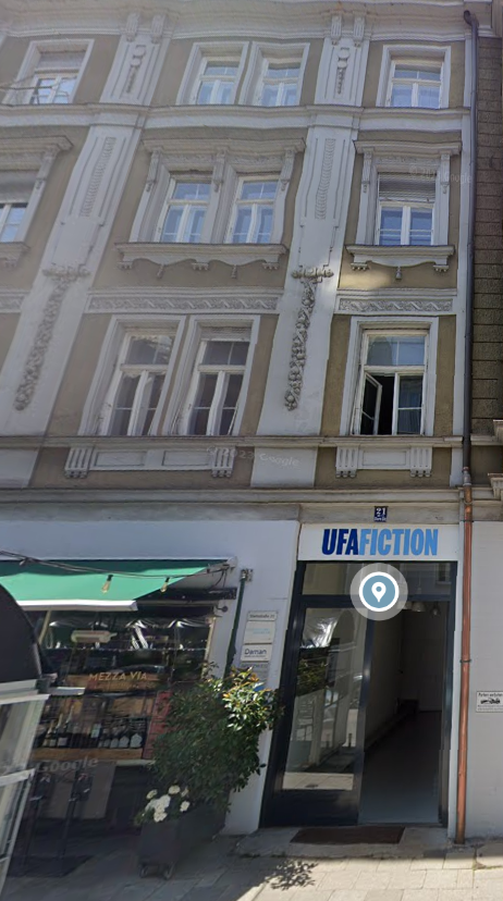 Mehrstöckiges Gebäude mit barocken Fassadendetails, neben einem Restaurant und einem offenem Eingang zur Sternstraße 21 mit der Aufschrift 'UFA Fiction' im Erdgeschoss.