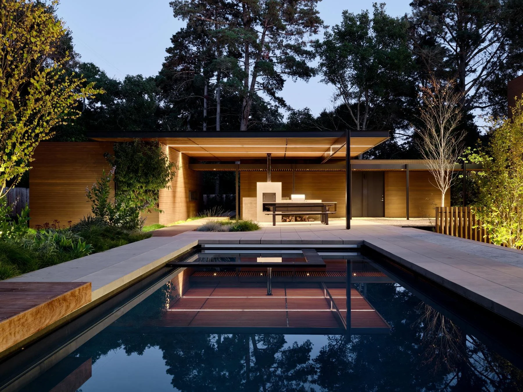 Sliding wood doors open the Atherton residence pool house to the patio and pool at dusk.