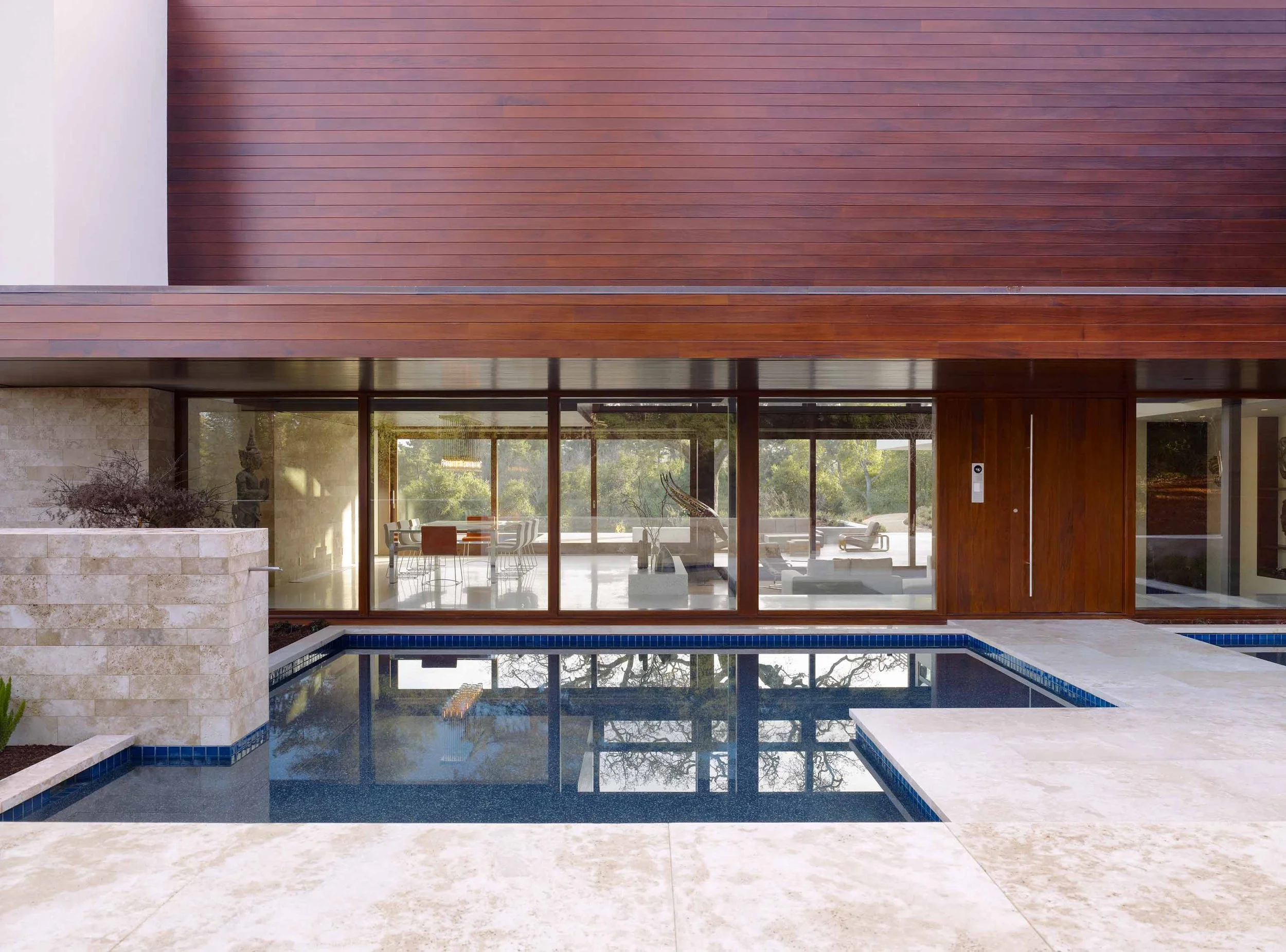 Wood-clad home exterior with glass walls opening onto a pool and travertine patio