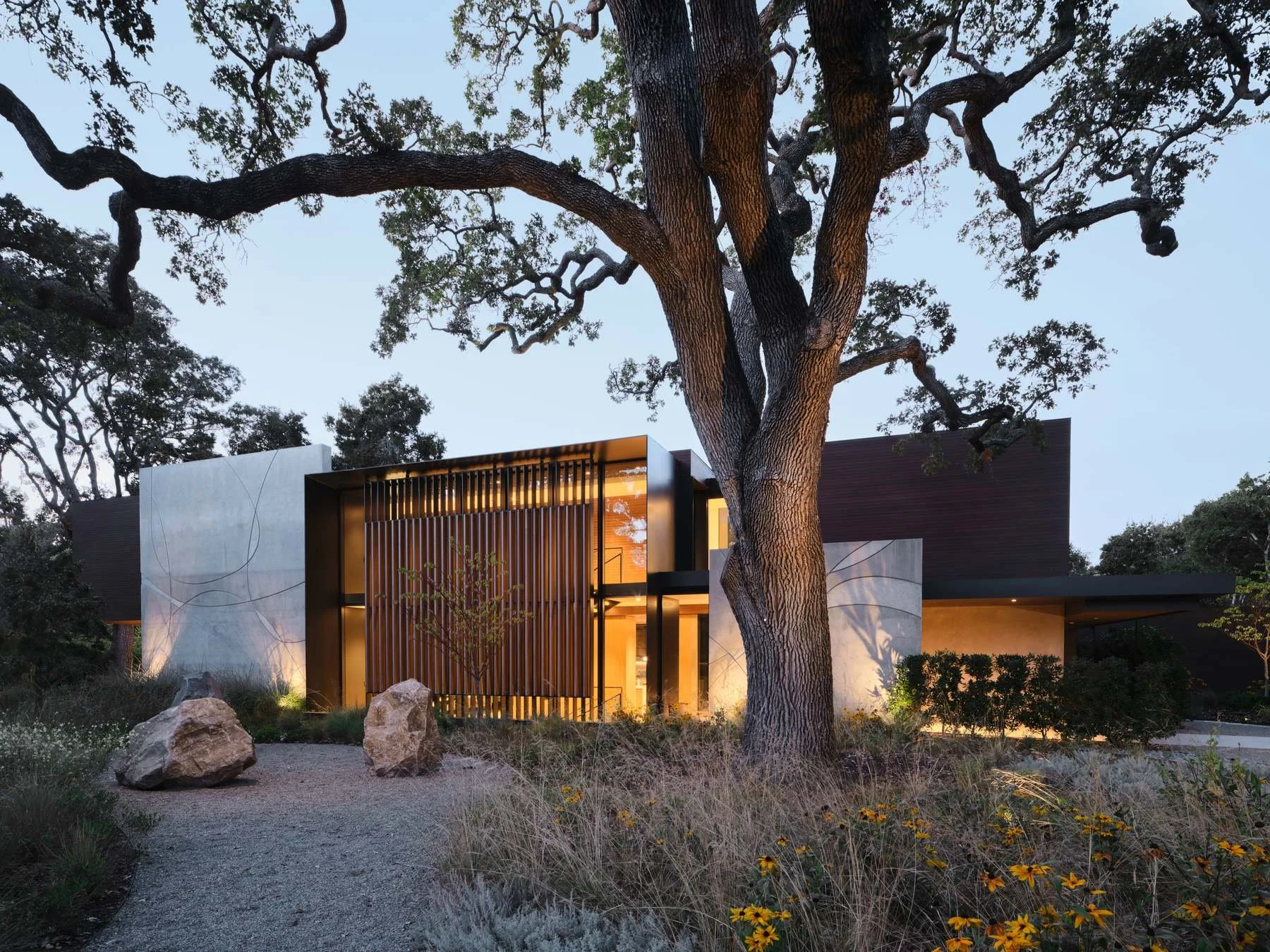 A custom wood entry door and steel windows glow at twilight at the atherton residence.