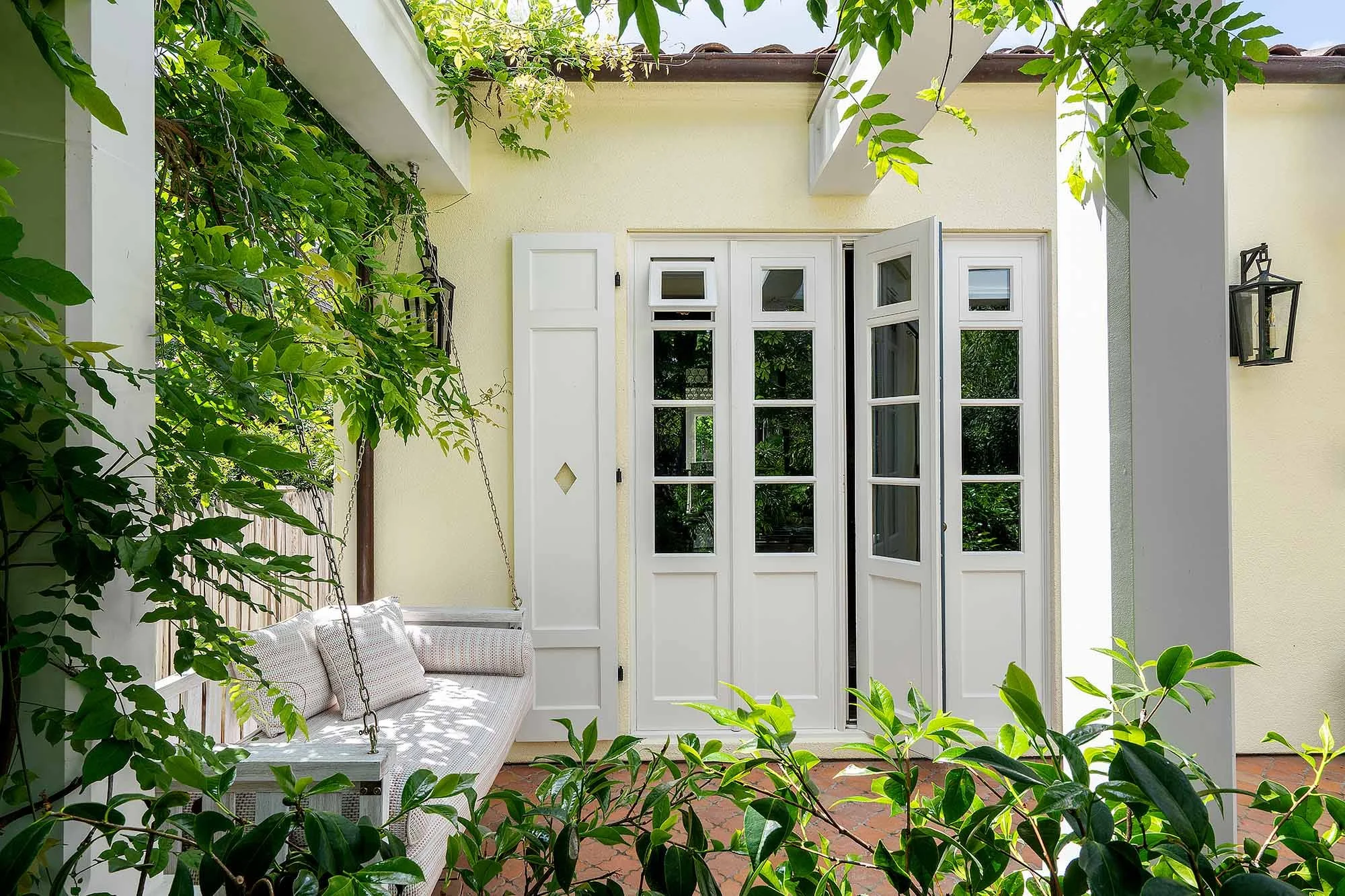 Custom white French doors opening to vine-covered courtyard with hanging porch swing
