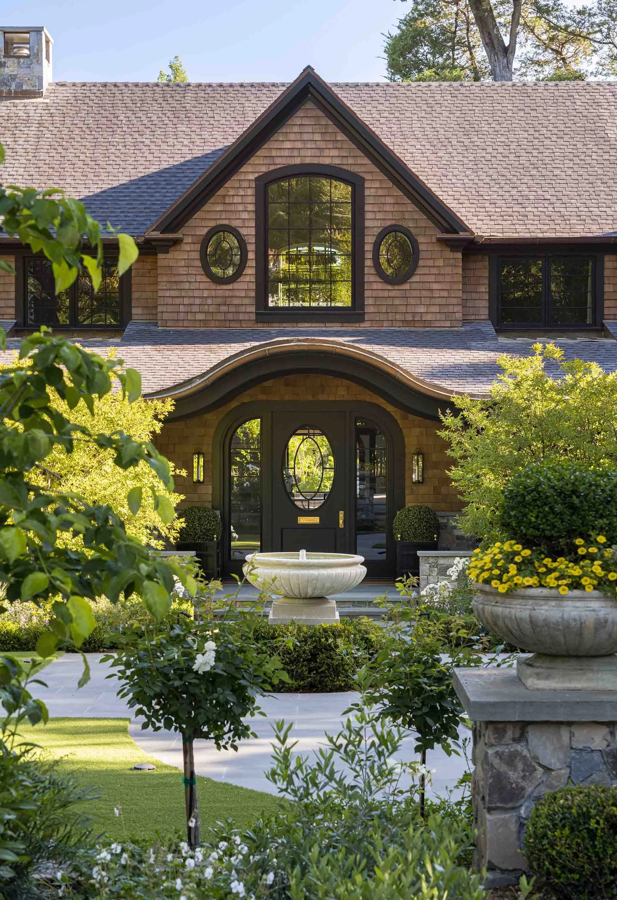 Handcrafted arched entry door with custom oval glass insert and sidelights, hand-fitted beneath a dramatic curved shingle portico — bespoke millwork by West Coast Architectural