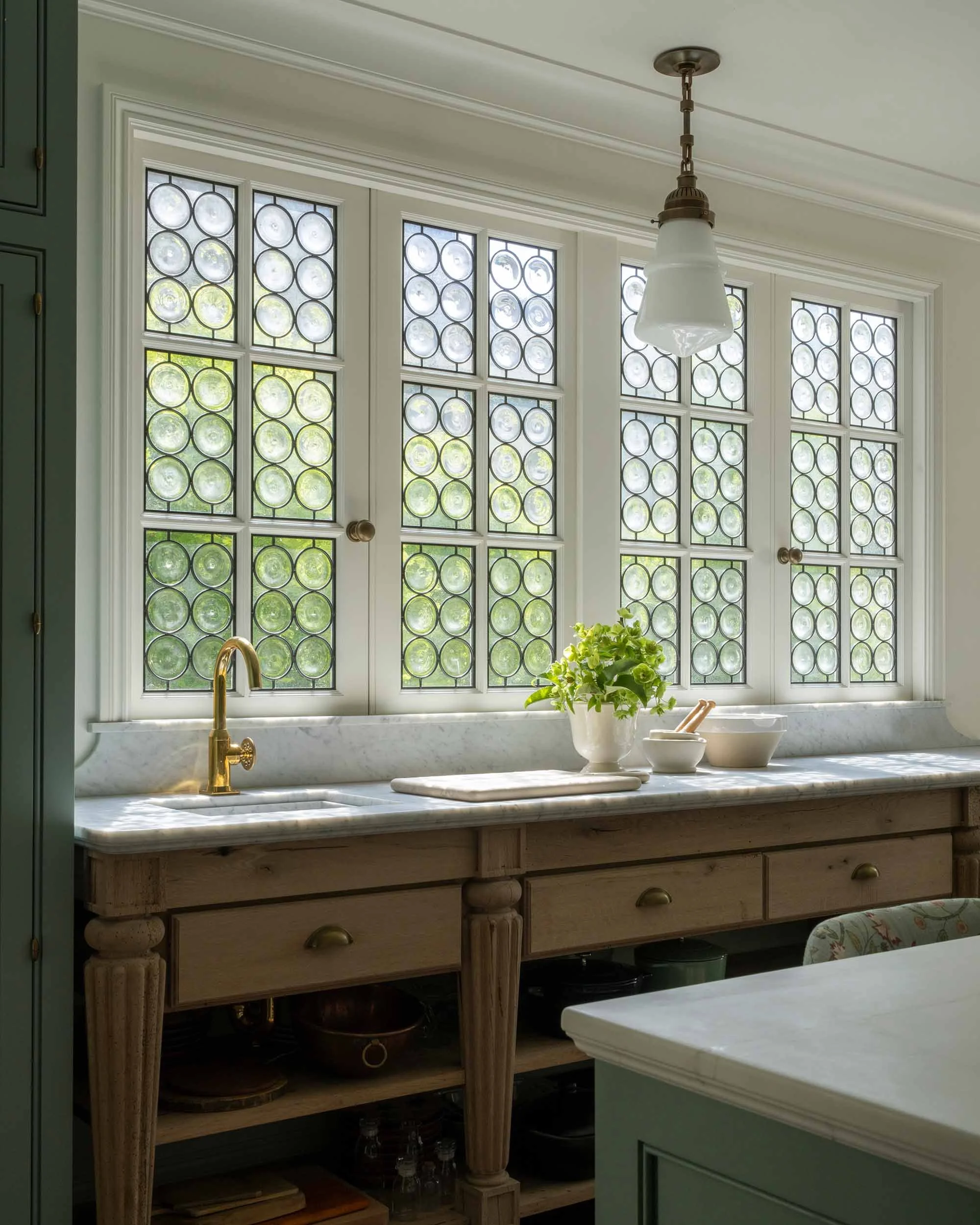 Custom bull's-eye leaded glass windows above marble sink with brass faucet in kitchen.