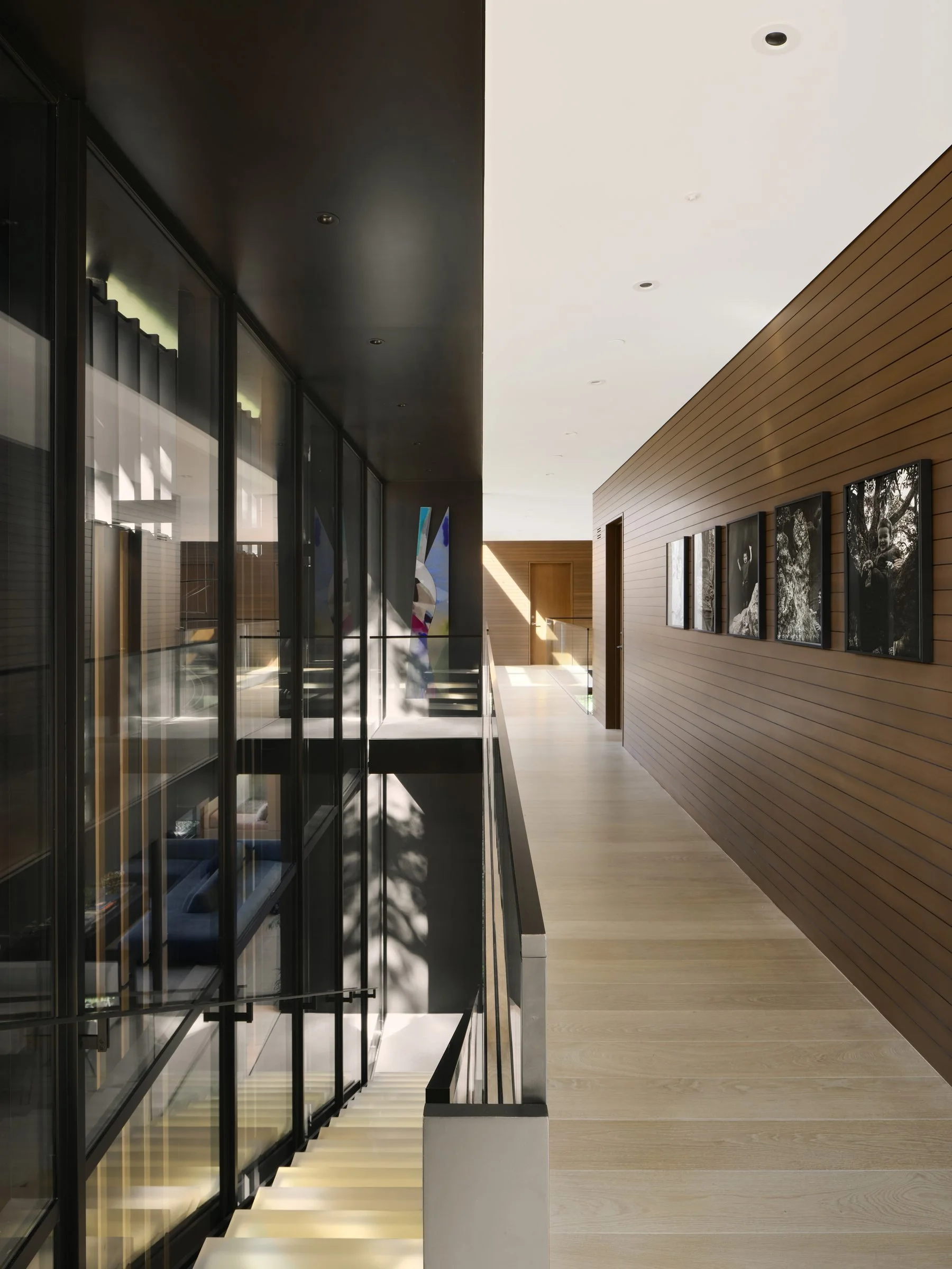 A custom glass wall system lines this Green Oaks hallway, opening views to the stairwell below.