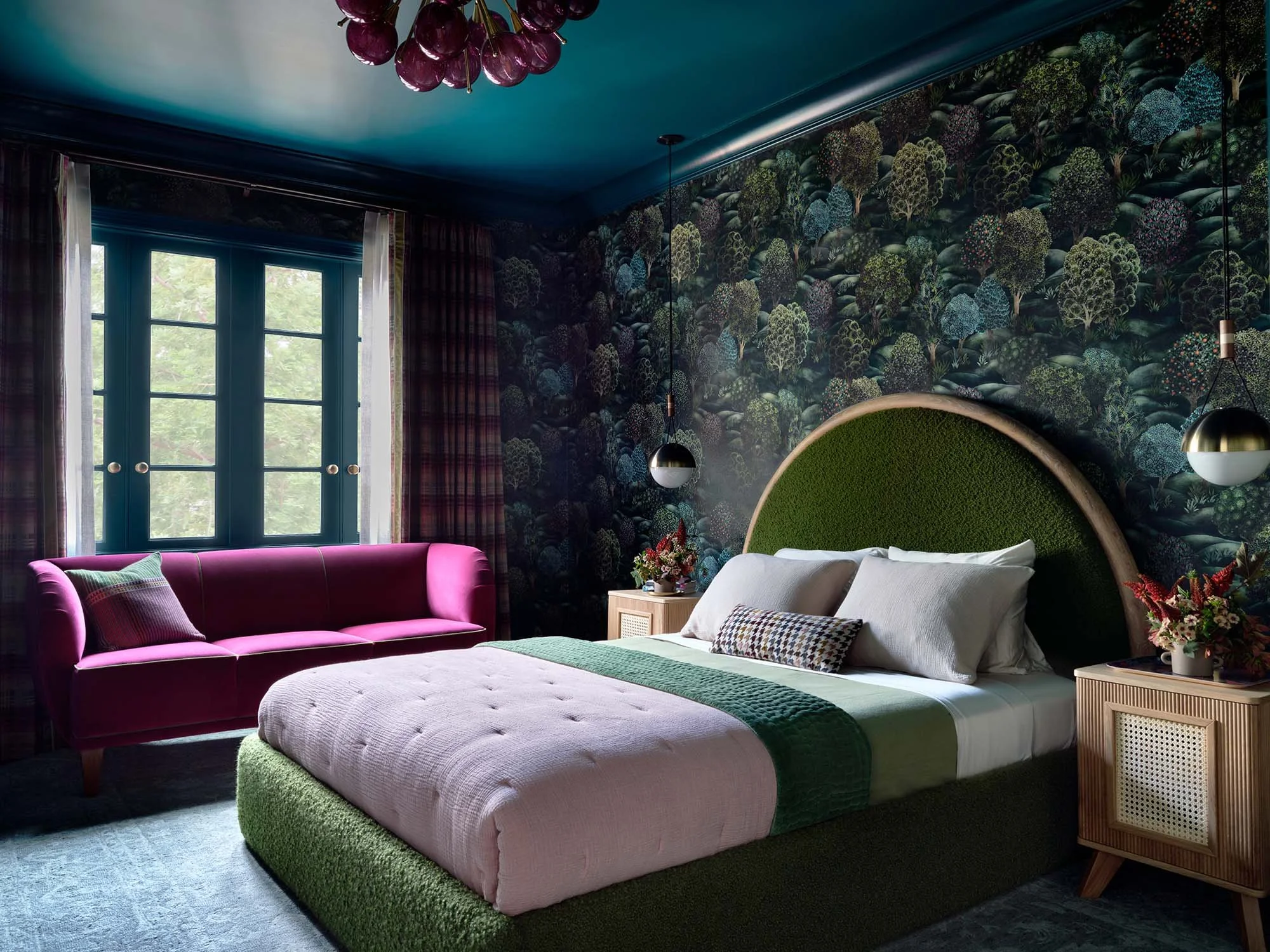 Custom teal-framed French doors in bold bedroom with arched green headboard and forest wallpaper.