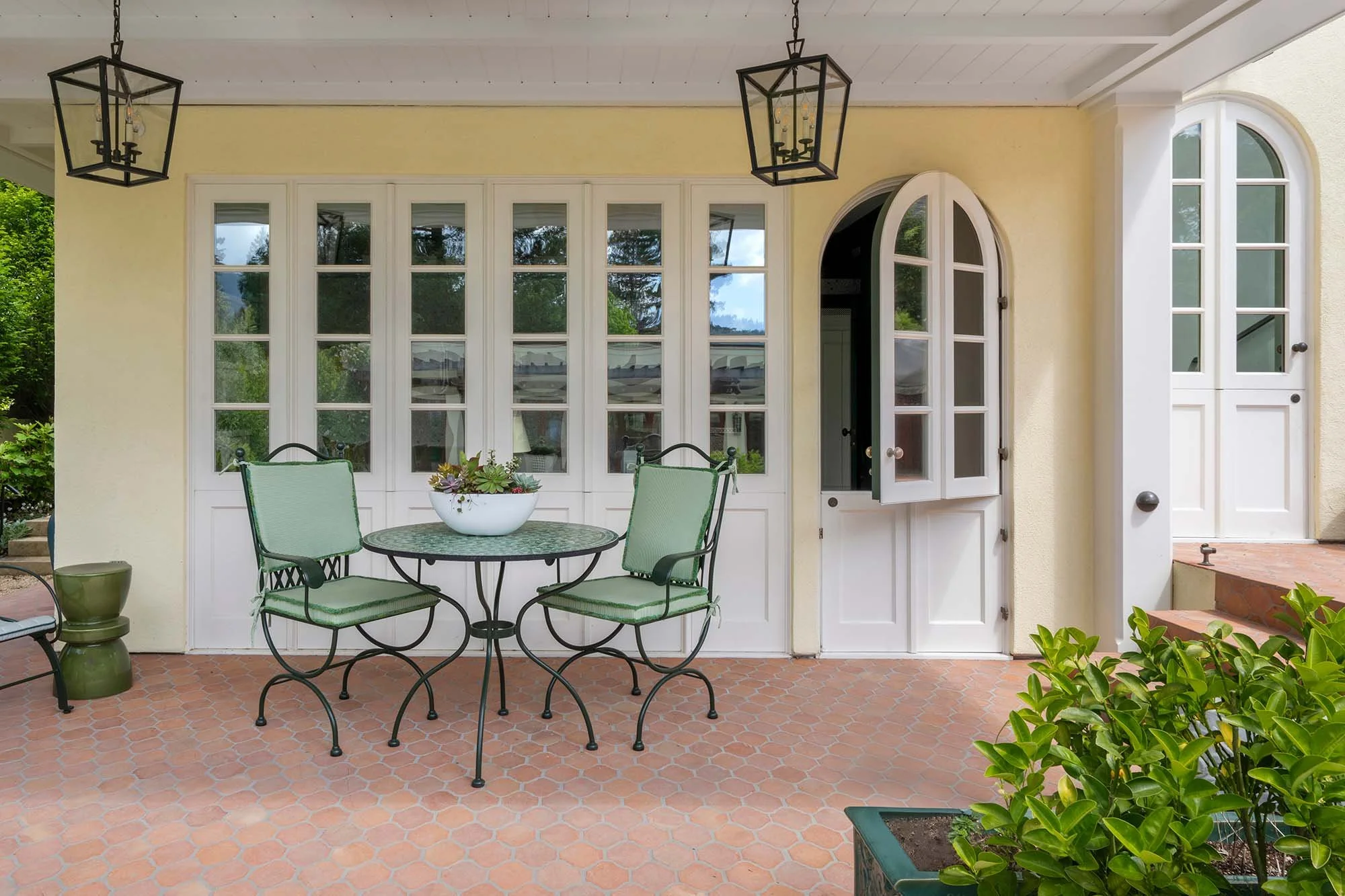 Custom white arched door and French doors on covered terracotta tile patio with bistro seating