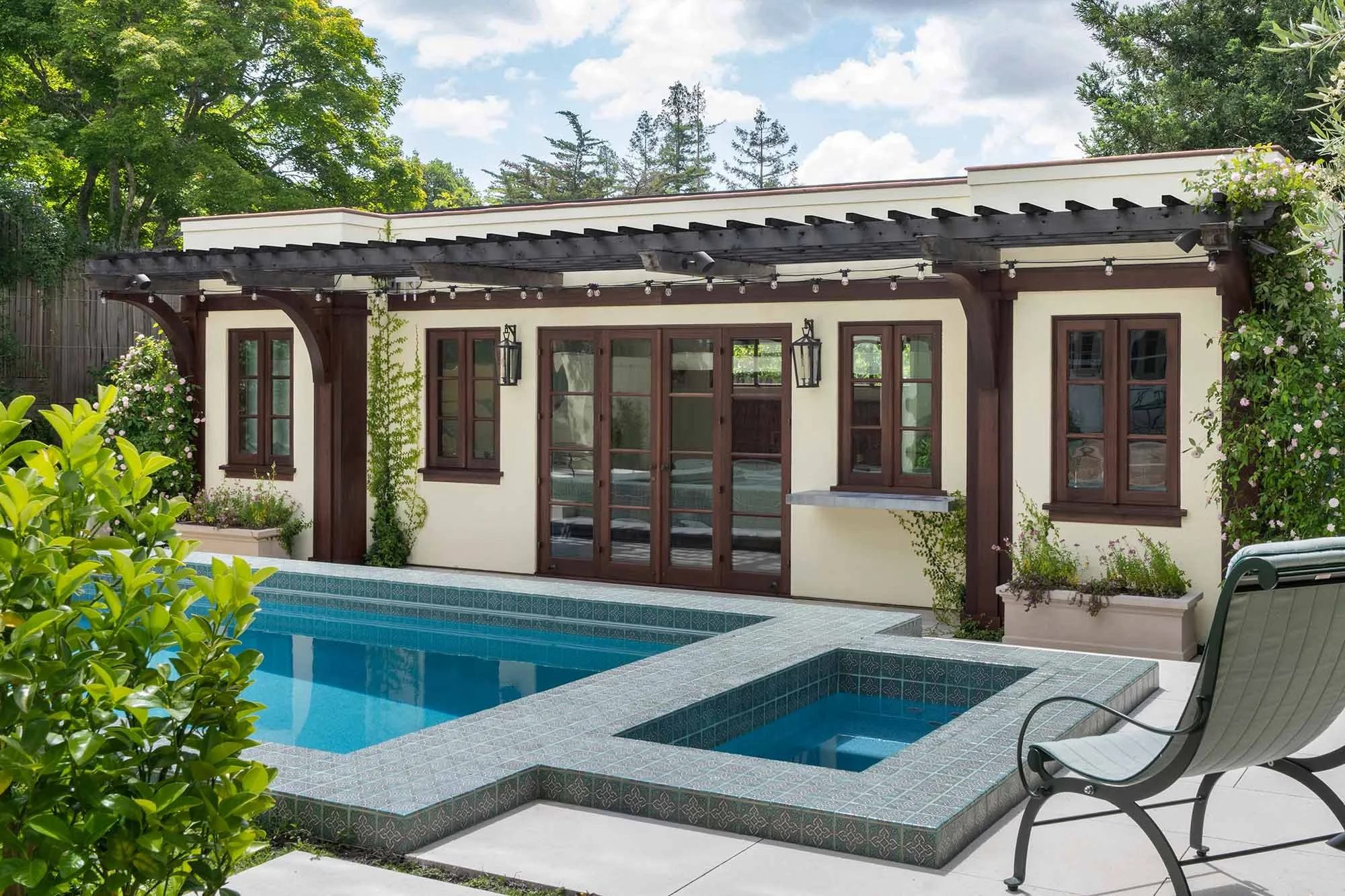 Custom dark wood-framed French doors and windows on Spanish-style pool house with pergola and pool.