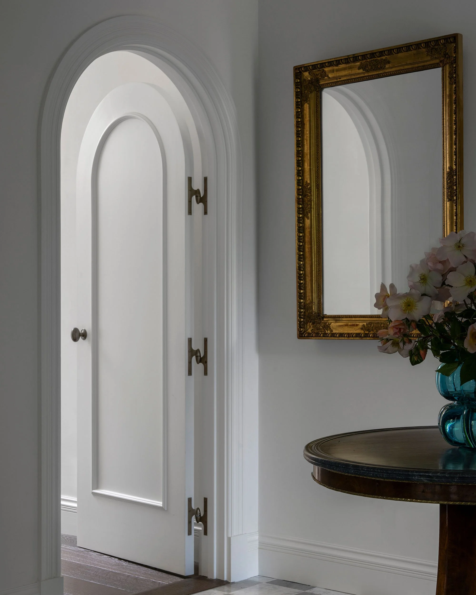White custom arched interior door with antique brass hook-and-eye hardware in hallway.