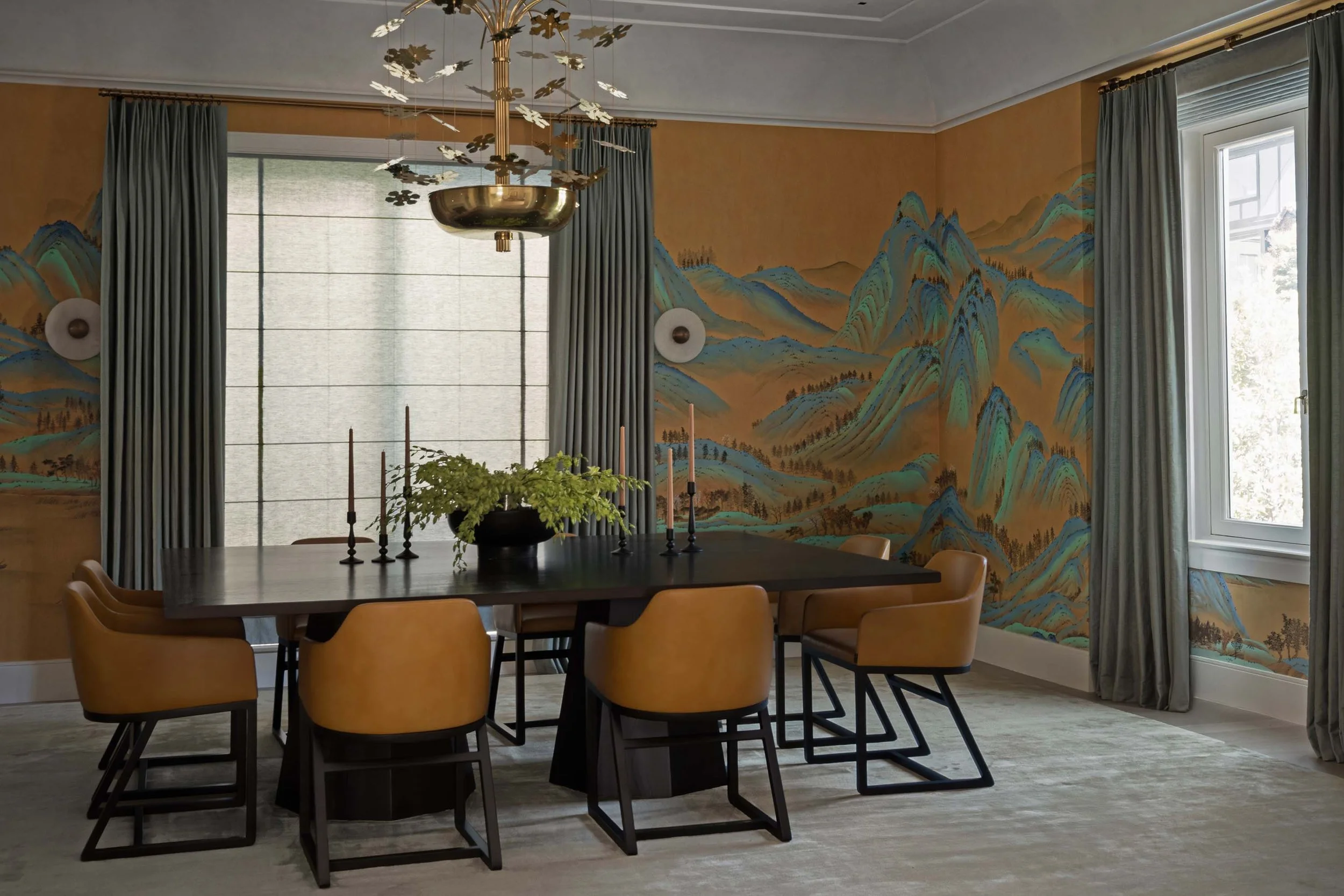 Dining table with taper candles beneath brass chandelier and mountain mural wallpaper