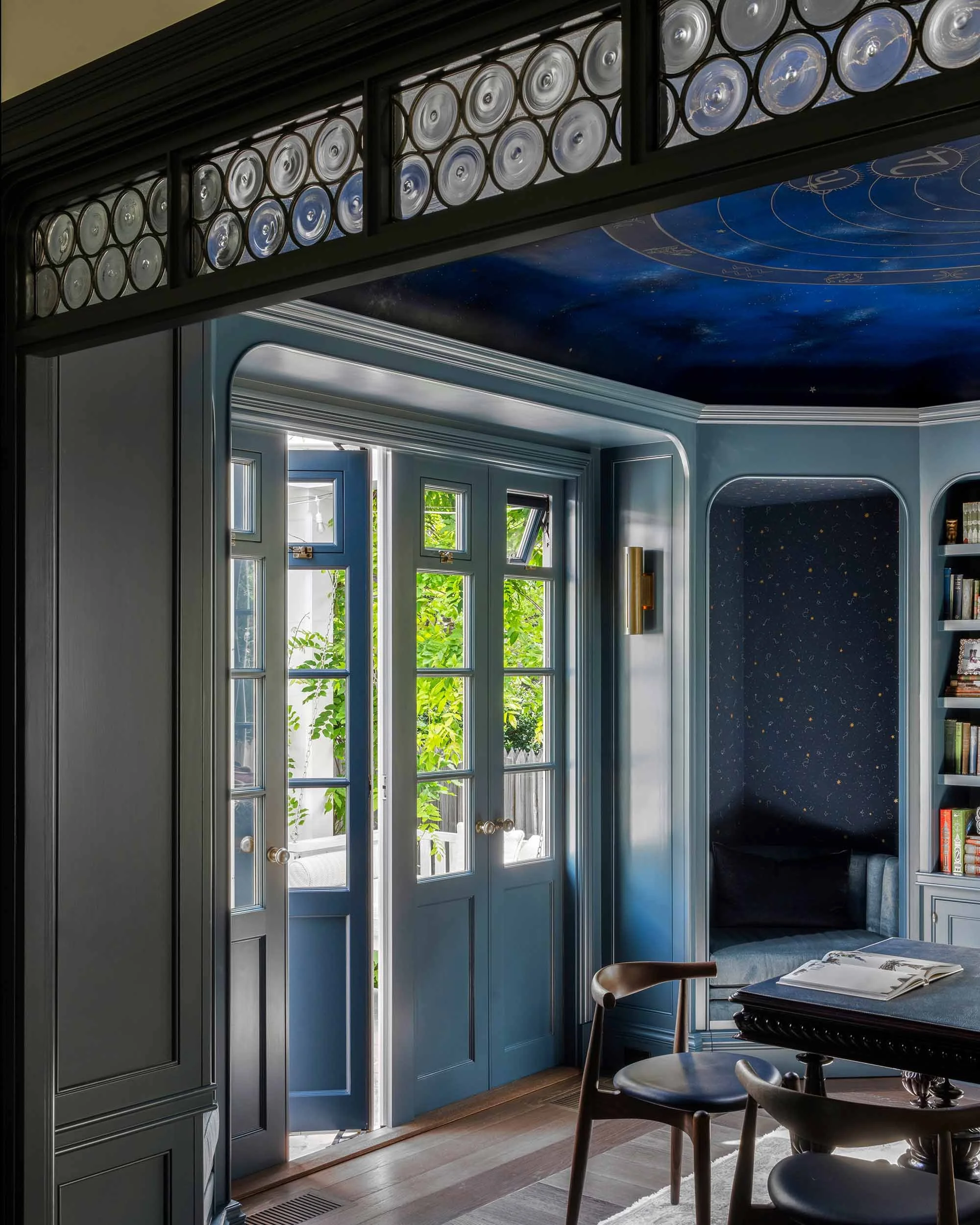 Leaded glass transom above blue French doors in navy study with hand-painted celestial ceiling. 