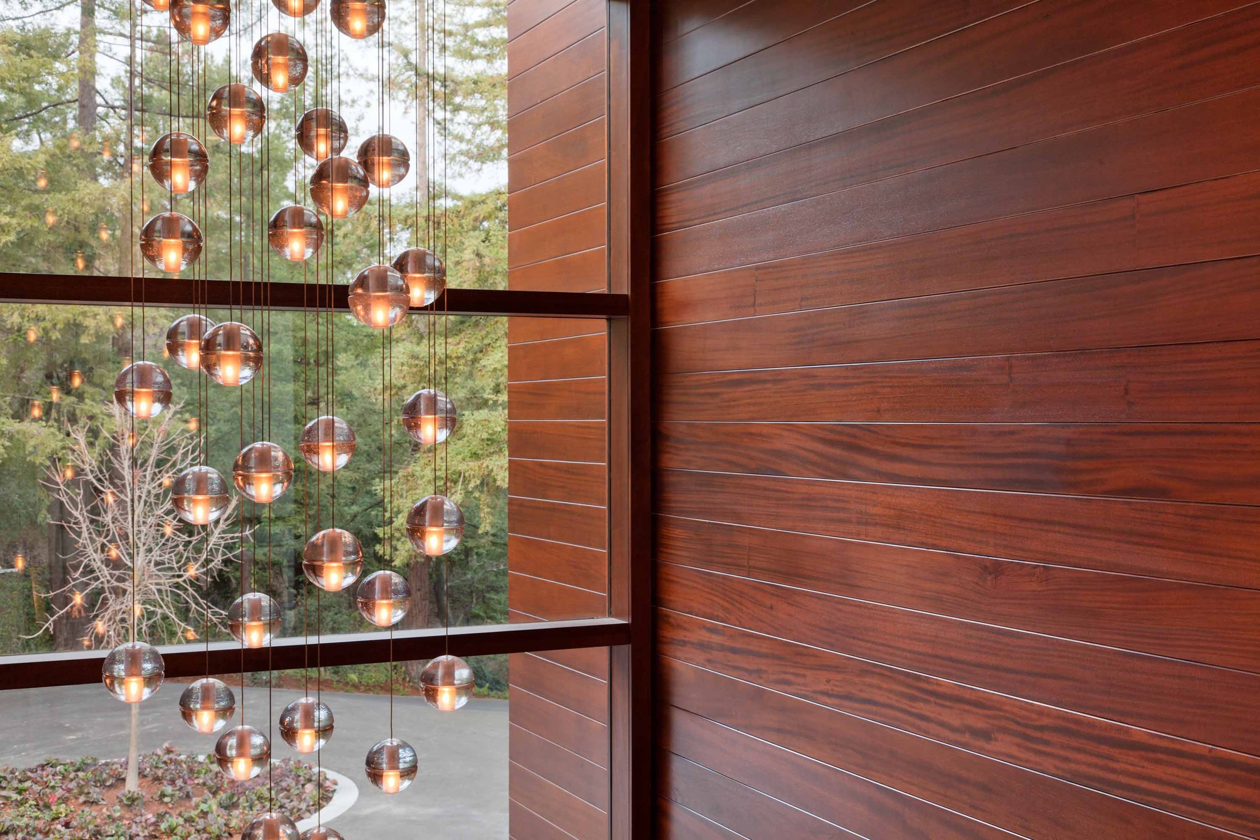 Glass bubble pendant chandelier hanging against a wood-paneled wall.