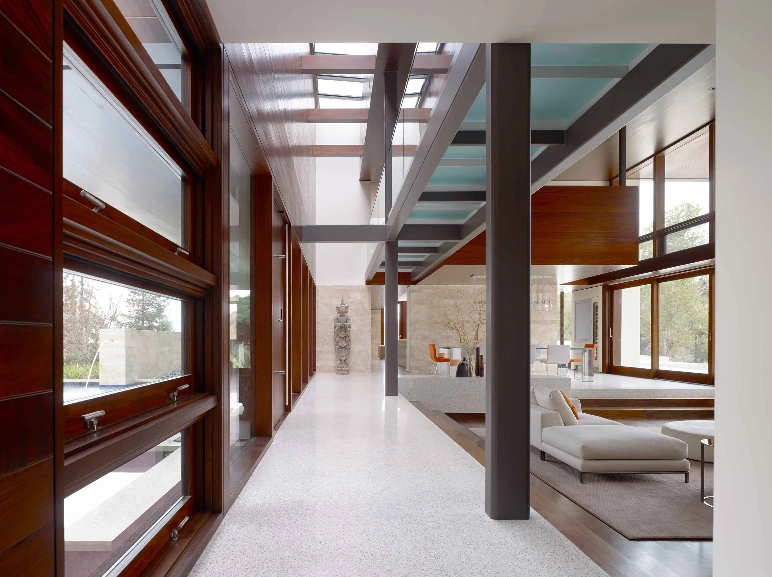 Long hallway with mahogany wood-clad walls, skylights, and a stone Buddha statue in a Silicon Valley residence