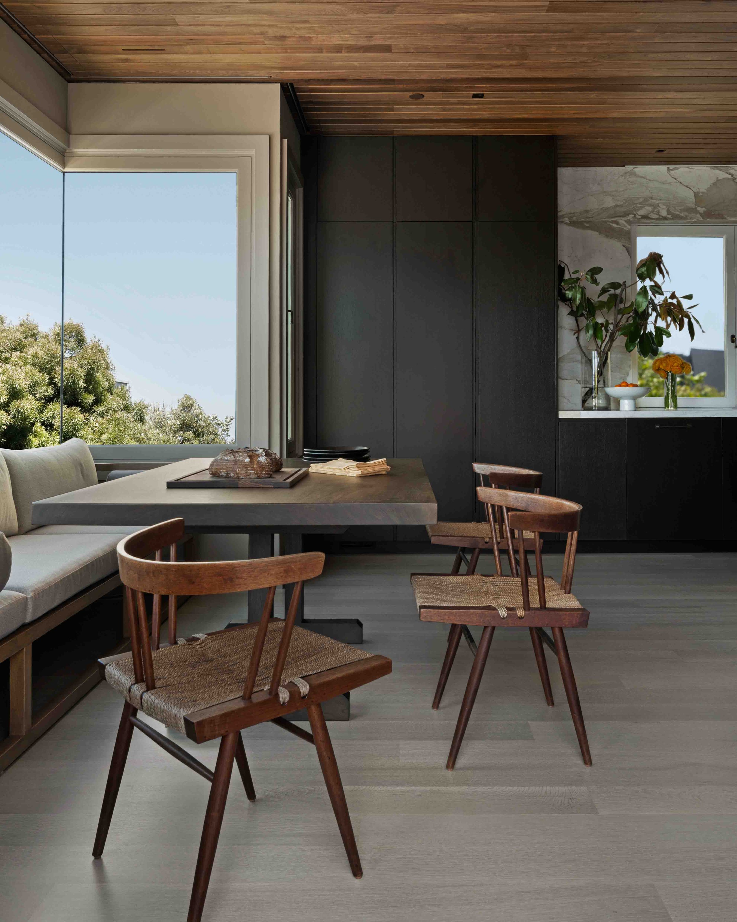 Dining nook with wishbone-style wood chairs and marble counter, black cabinetry in background