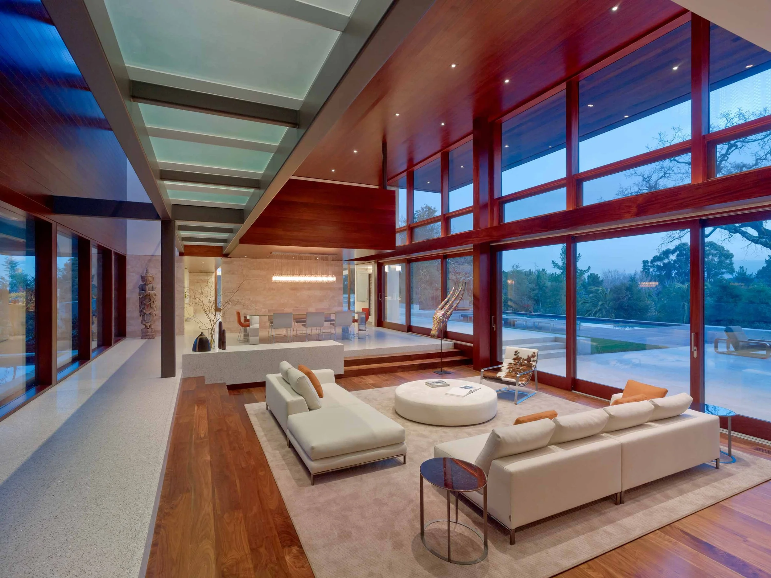 Living room at dusk with floor-to-ceiling glass walls and a mahogany wood ceiling.