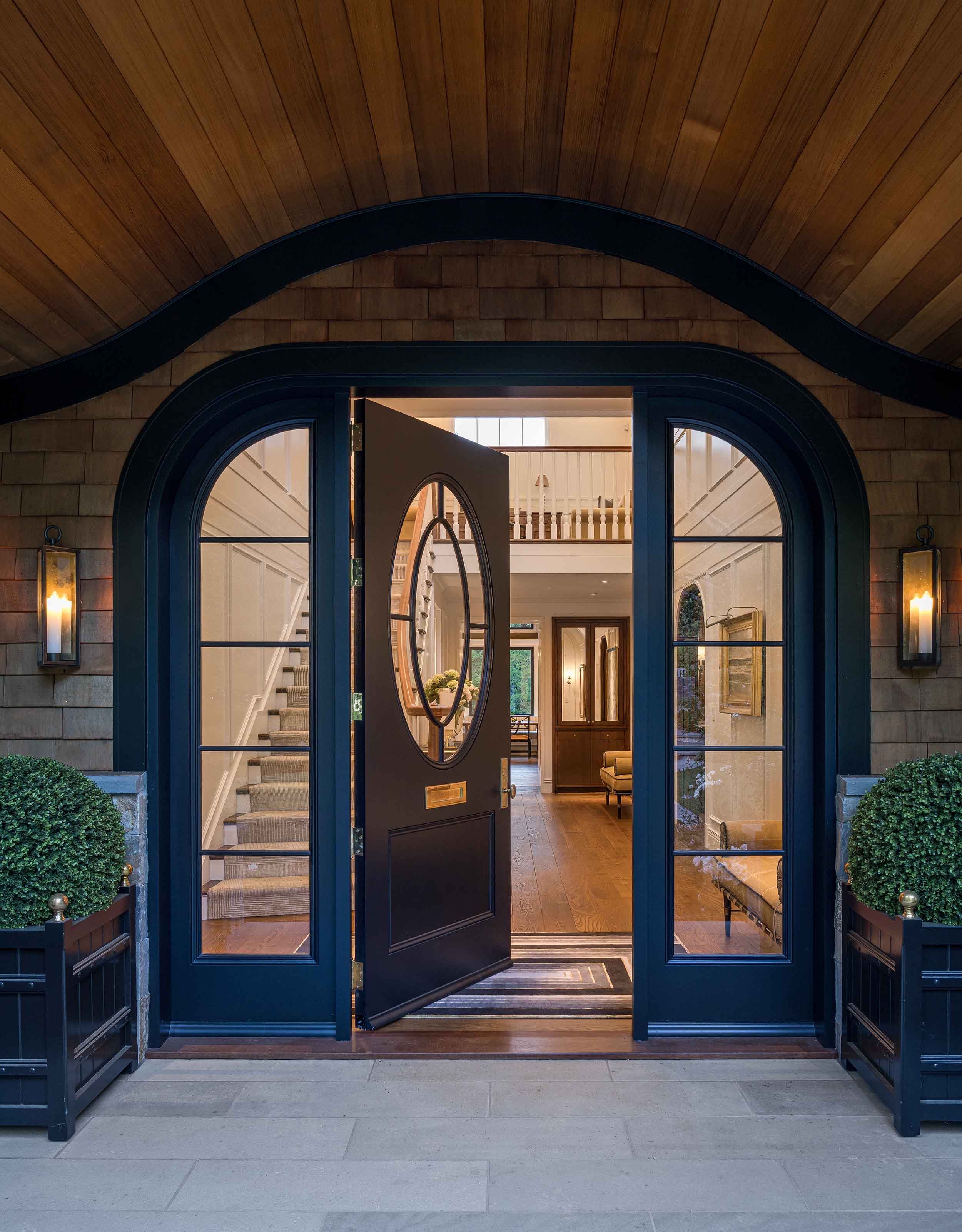 Custom navy arched entry door with oval leaded glass window and matching sidelights, open to reveal a grand foyer — crafted by West Coast Architectural