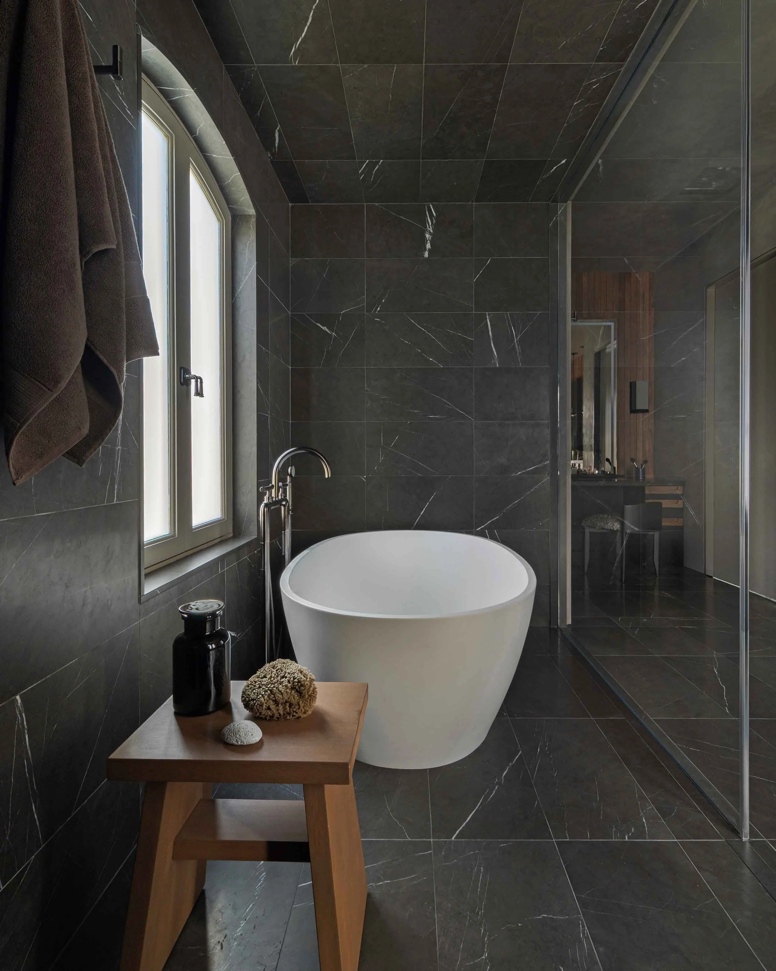 Freestanding round soaking tub in dark marble bathroom with arched window