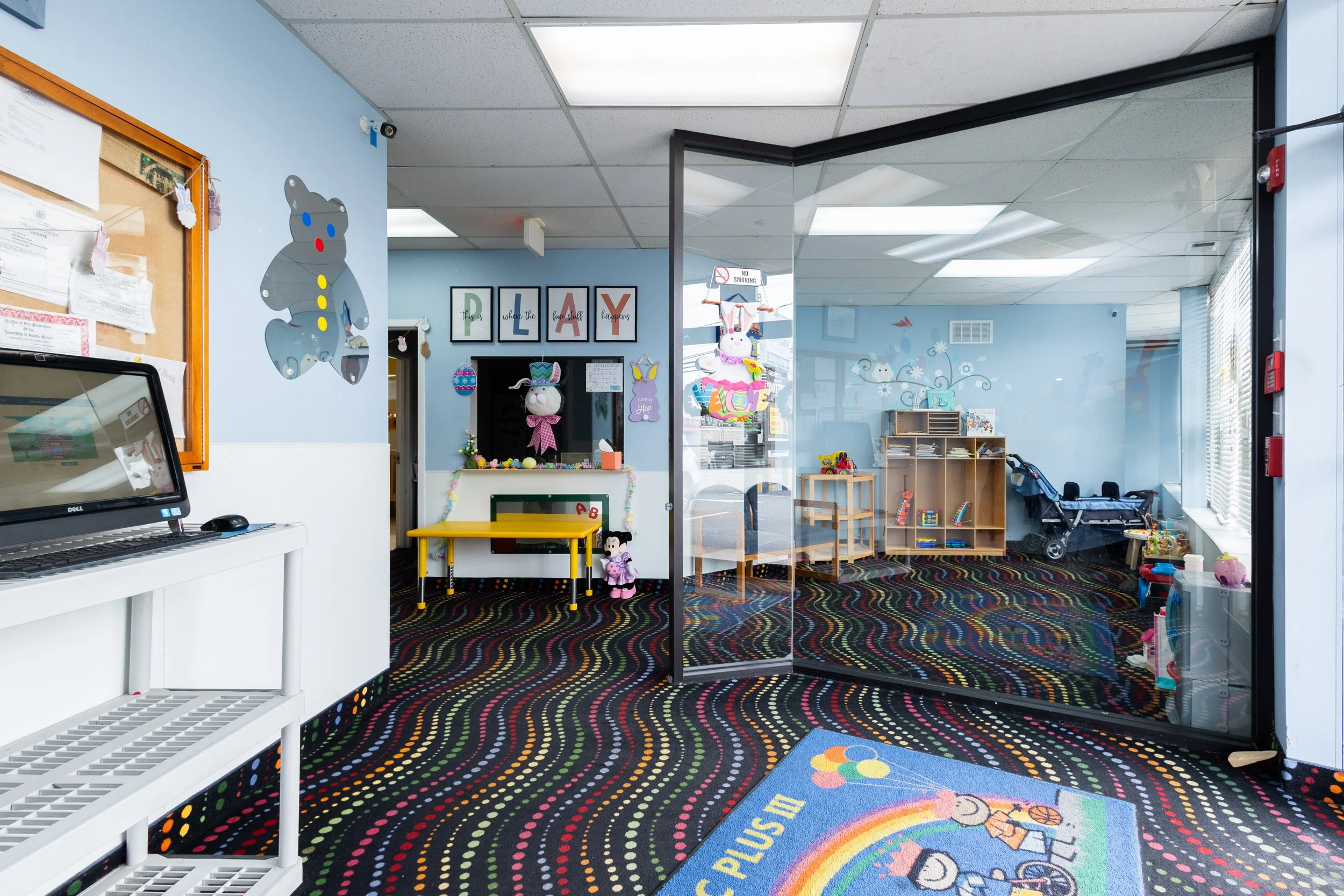 Lobby view of TLC Plus Daycare located in Saddle Brook, NJ. The images include an inviting play area on the right and a service window with an assortment of cheerful decorations. TLC Plus Daycare and Preschool cares for children up to 5 years old.