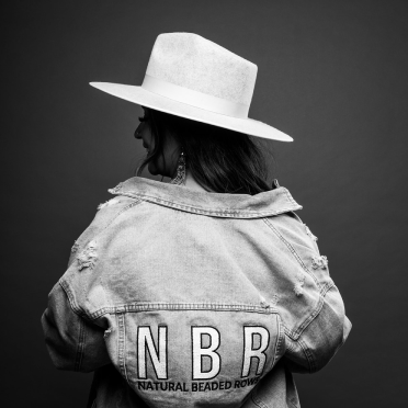 Back view of a woman wearing a wide-brimmed hat and a denim jacket with an 'NBR' logo.