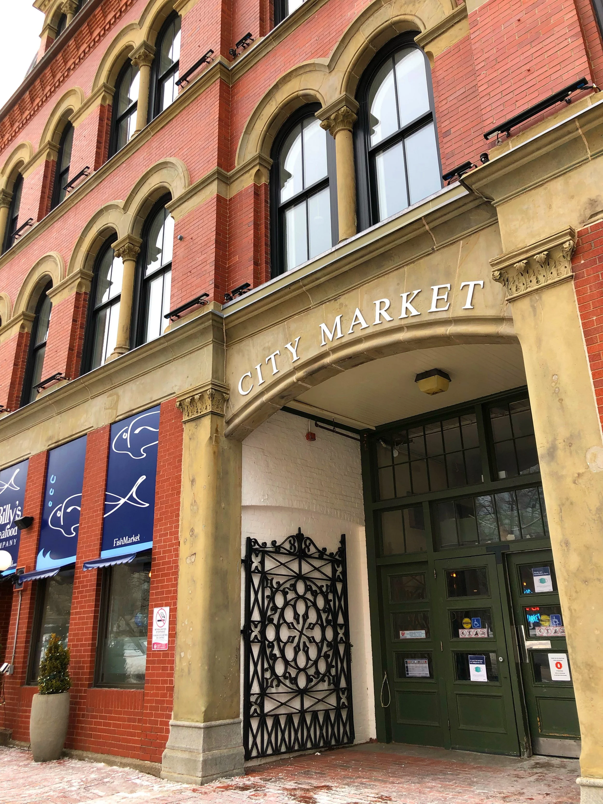 Entrance to the Saint John City Market, featuring brick and stone facade, large windows, and decorative ironwork gate.