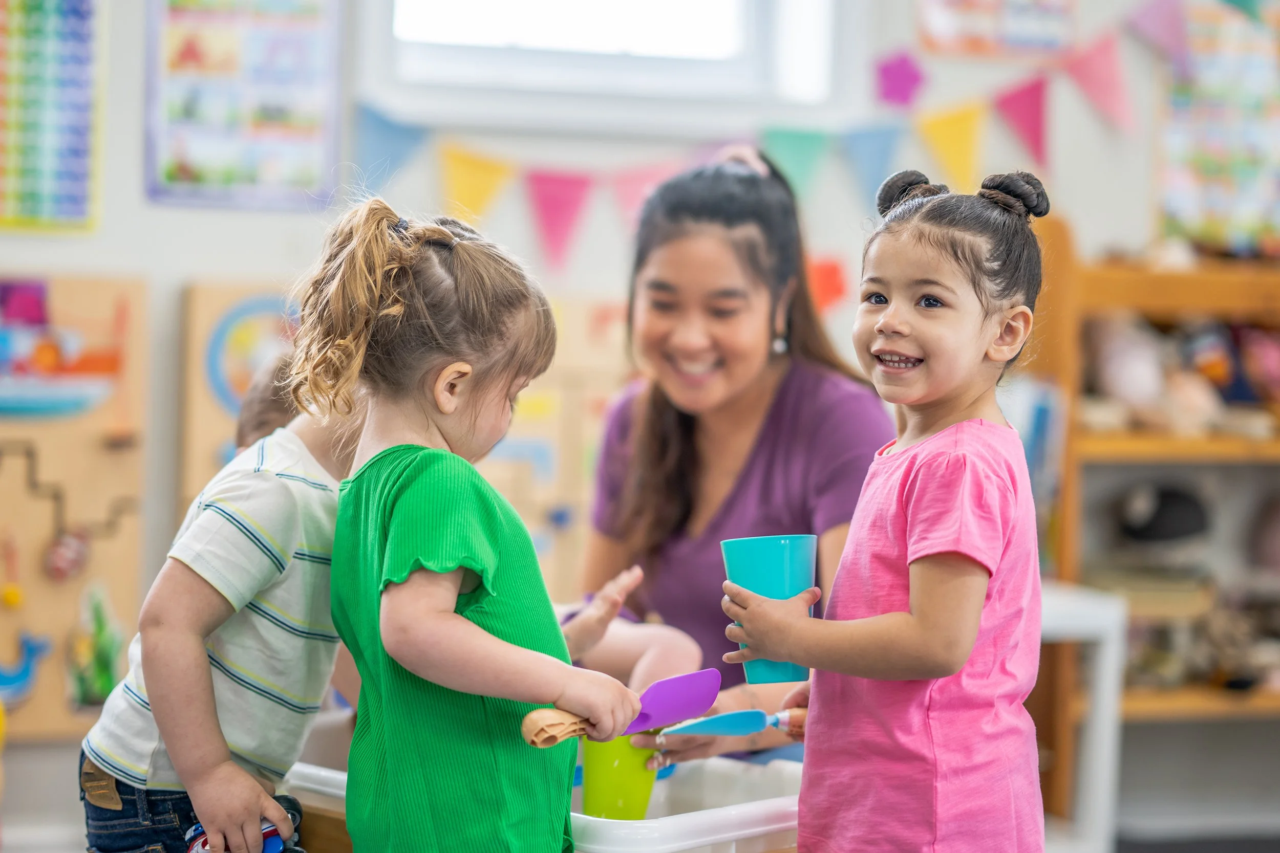 Children playing with toys and a teacher in a colorful daycare classroom.