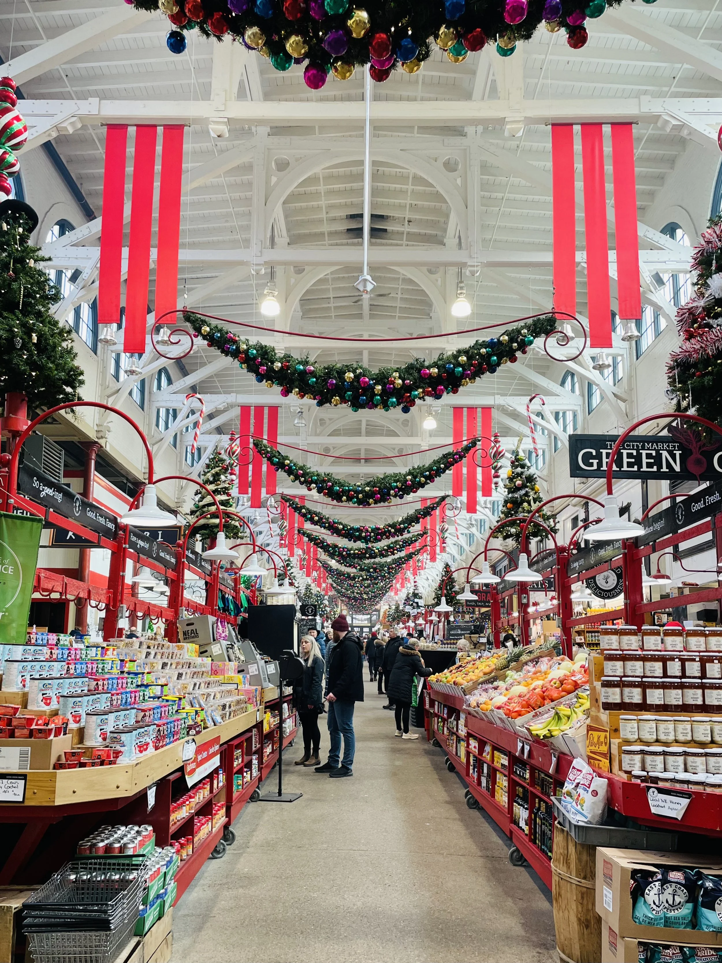 Inside the Saint John City Market decorated for Christmas with red banners, green garlands with ornaments, and Christmas trees.