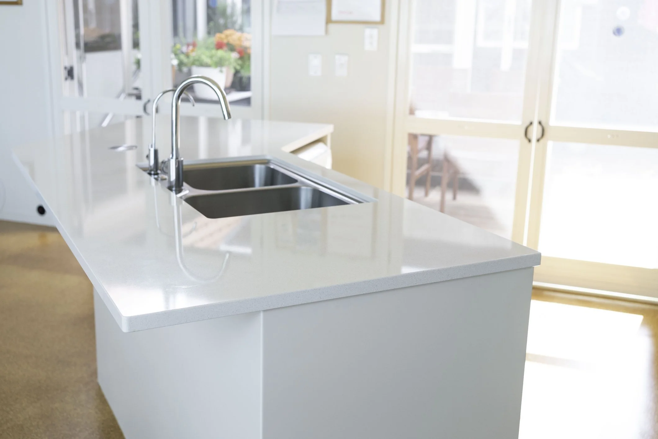 Kitchen island with a double sink and chrome faucet in a bright room with sliding glass doors and potted plants outside.