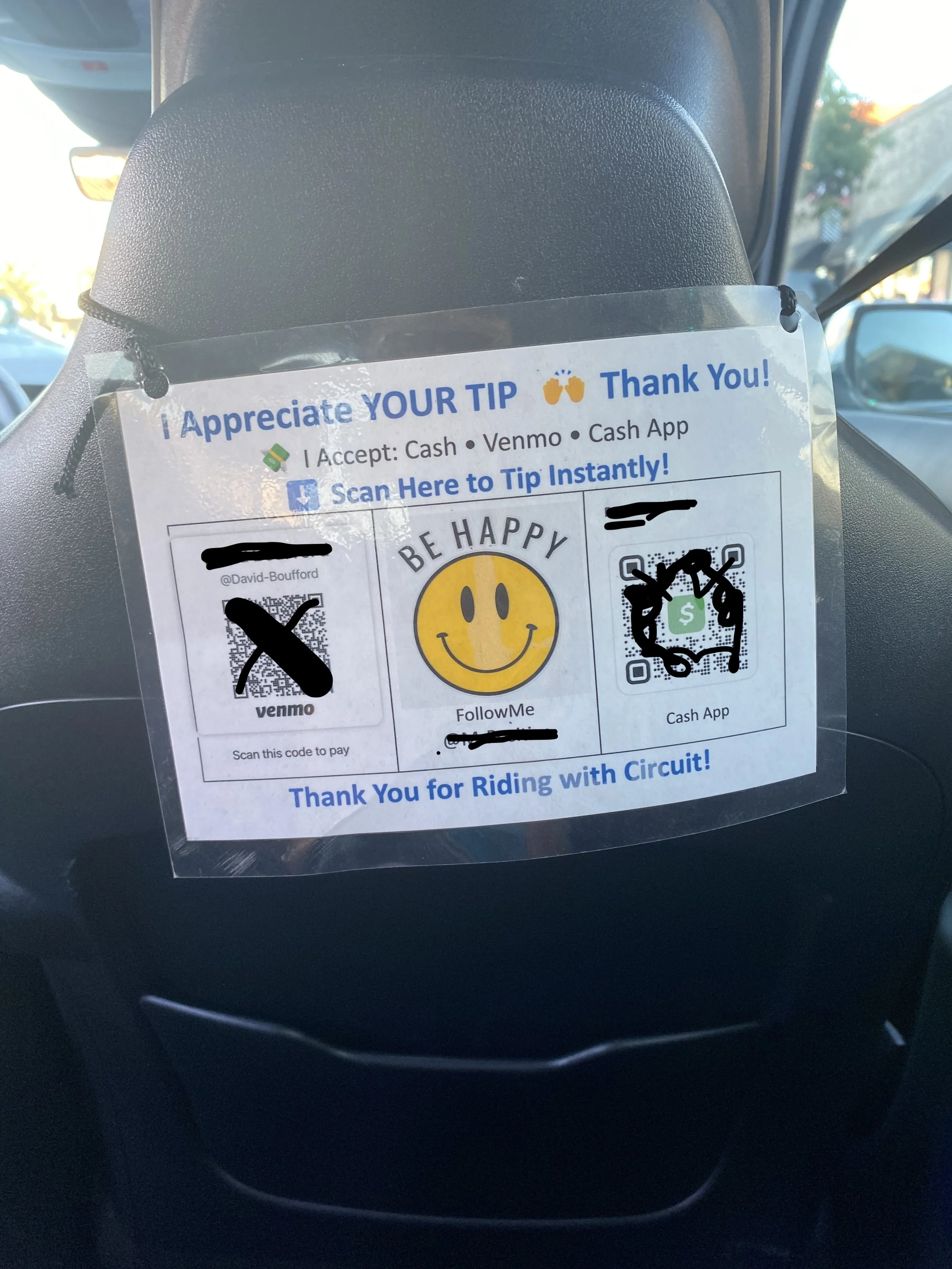 Image of back of the passenger seat of a car with a hand made sign hanging off of. the back of it that says "I appreciate your tip thank you! I accept cash, venmo, cash app. With QR codes and underneath says "Thank you for riding with Circuit!"