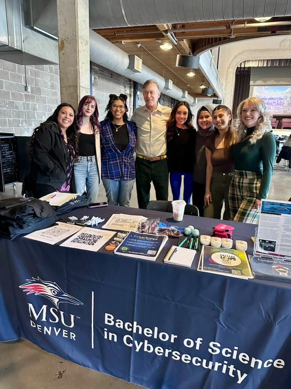 Whitney Haddad and student group members standing at an MSU Denver Cybersecurity booth with Senator Hickenlooper.